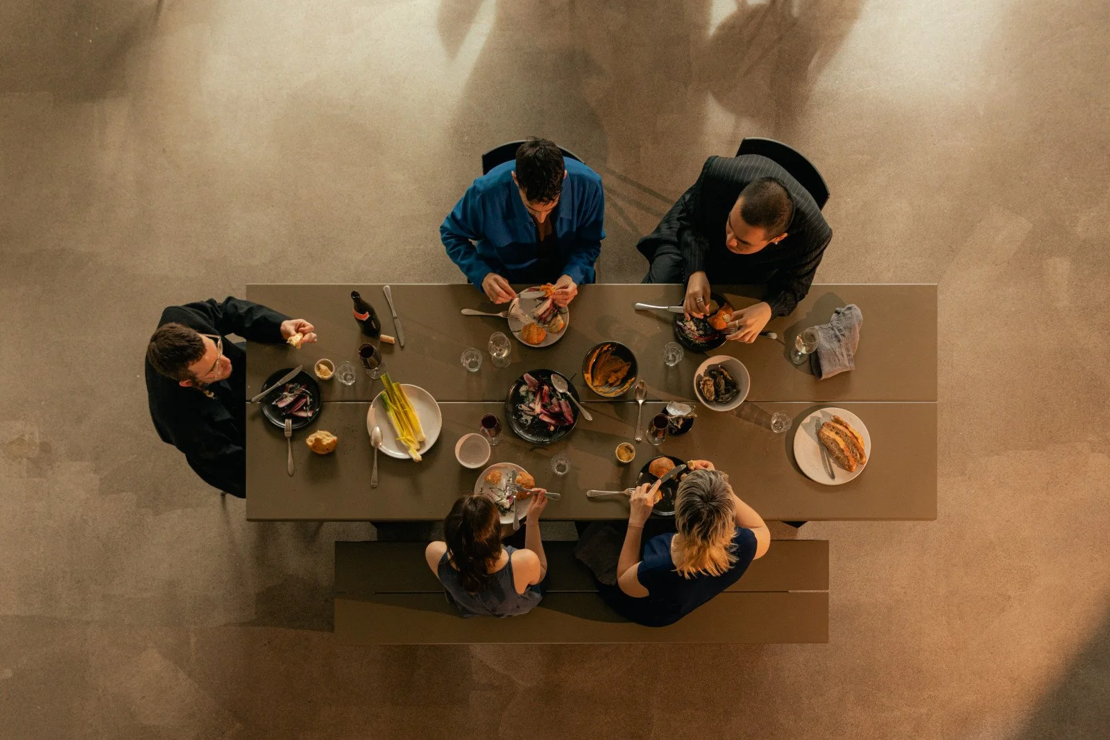 A top-down view of a long banquet table set for a gathering or dinner, with chairs on either side, decorated with candles, flowers, and various dishes in bowls and plates.