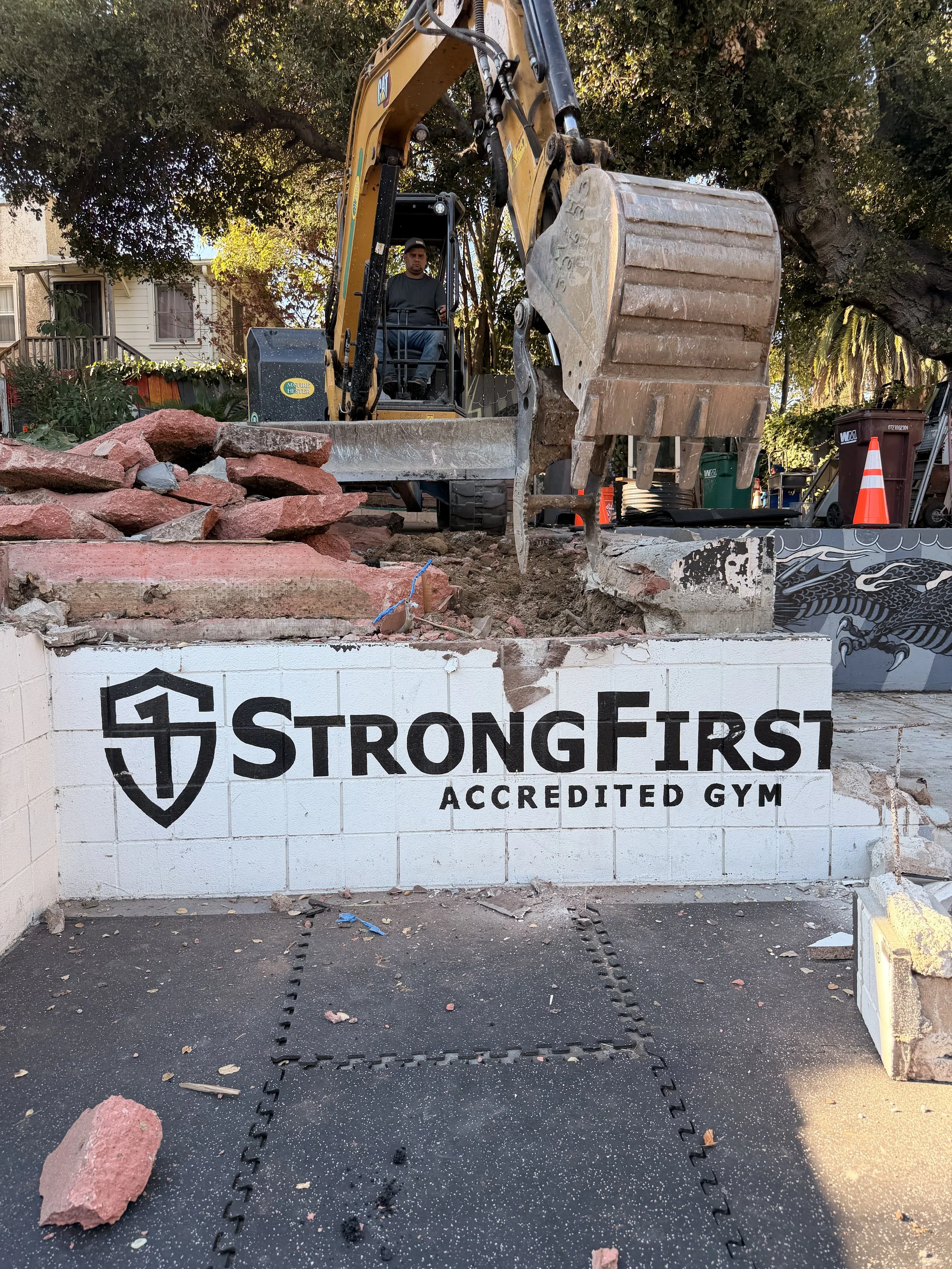StrongFirst Accredited Gym wall at OMP’s Dimond District site with an excavator breaking ground on the rebuild