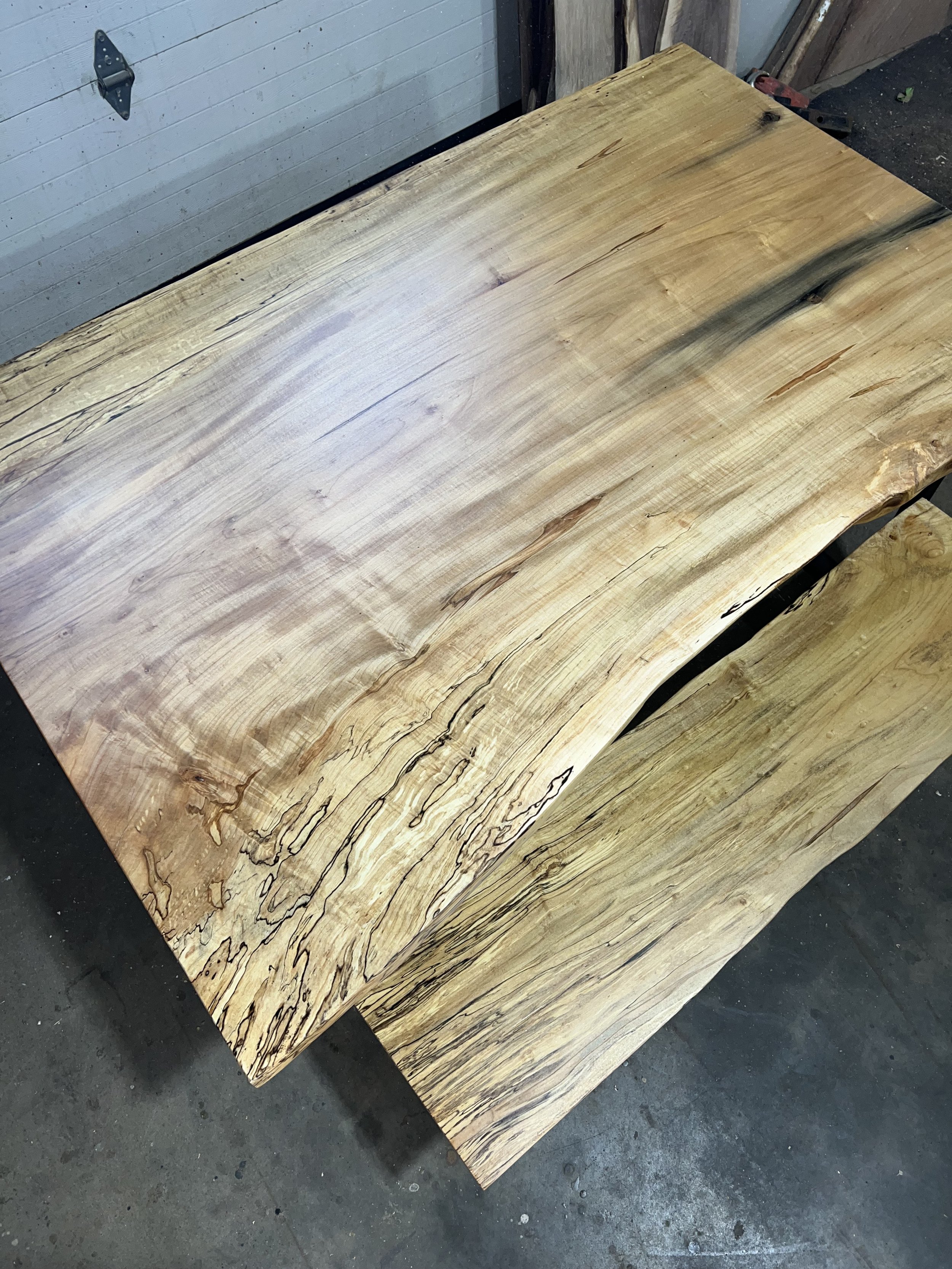 Close-up of a large, smooth wooden table with natural grain and imperfections placed on a concrete floor.