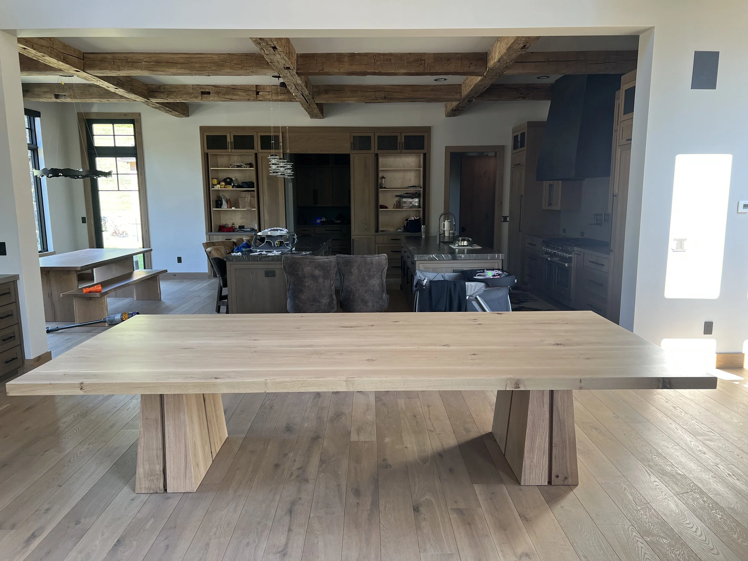 Unfinished kitchen with a large wooden dining table and a kitchen island, open concept with exposed wooden beams, large windows, and modern grey cabinets.