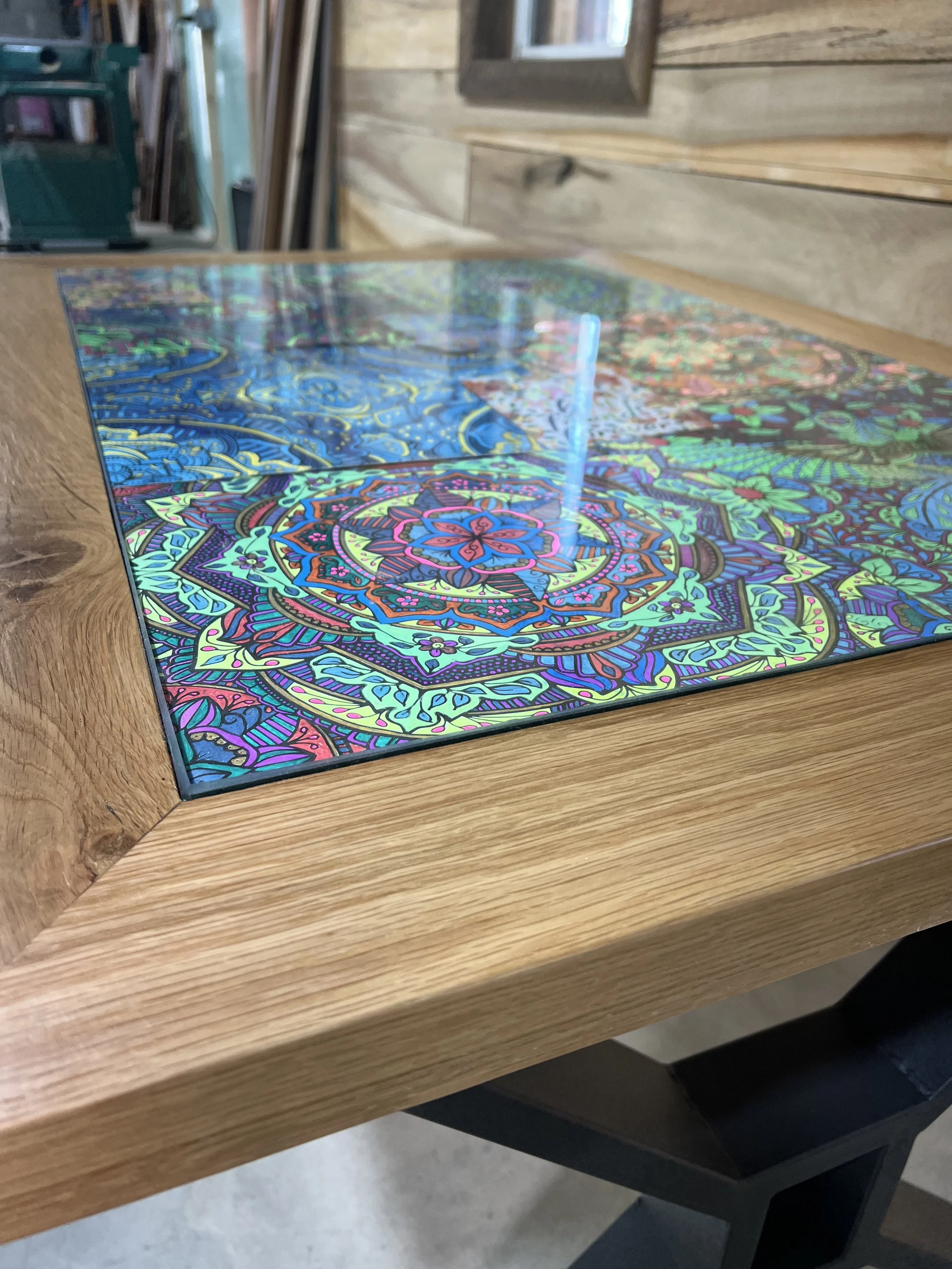 Colorful, intricate mandala design on a glass surface placed on a wooden table.