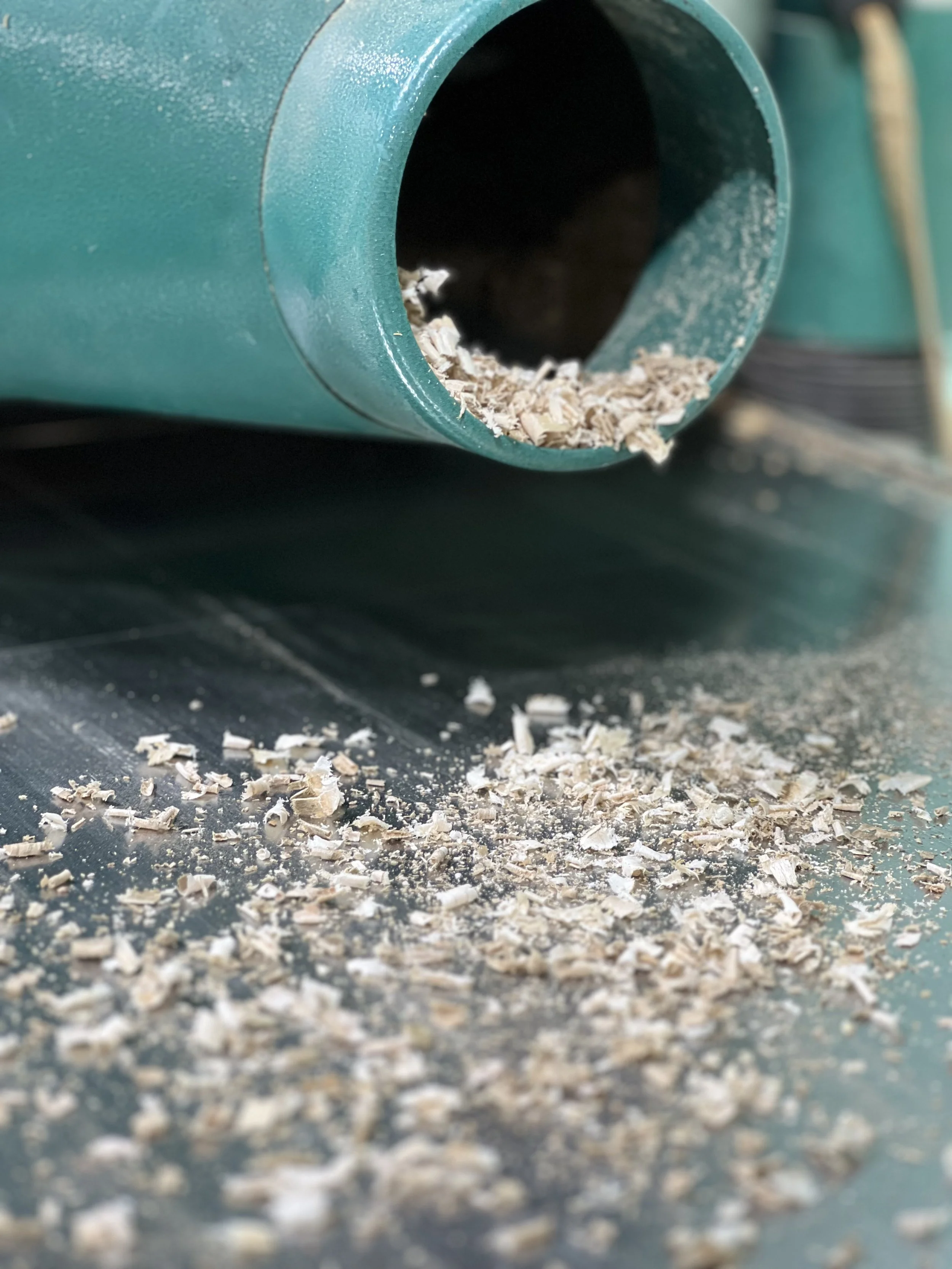 Wood shavings and sawdust coming out of a green woodworking machine or planer onto a metal surface.