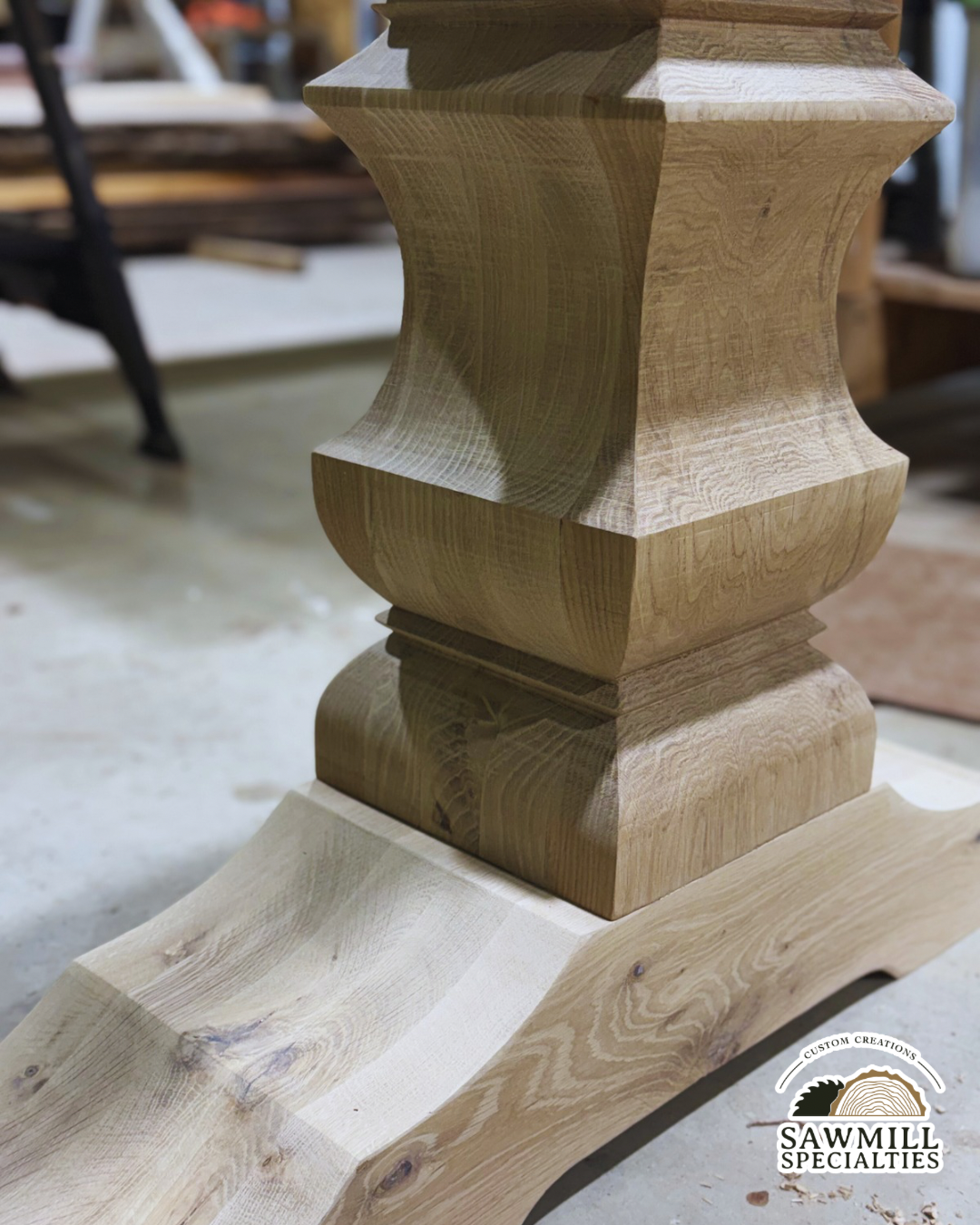A close-up of a wooden stand or furniture piece with a decorative, carved design. The wood has a natural finish, showcasing its grain and texture. In the background, woodworking tools and materials are visible, indicating a woodworking shop setting. The logo of 'SawMill Specialties' is in the lower right corner.