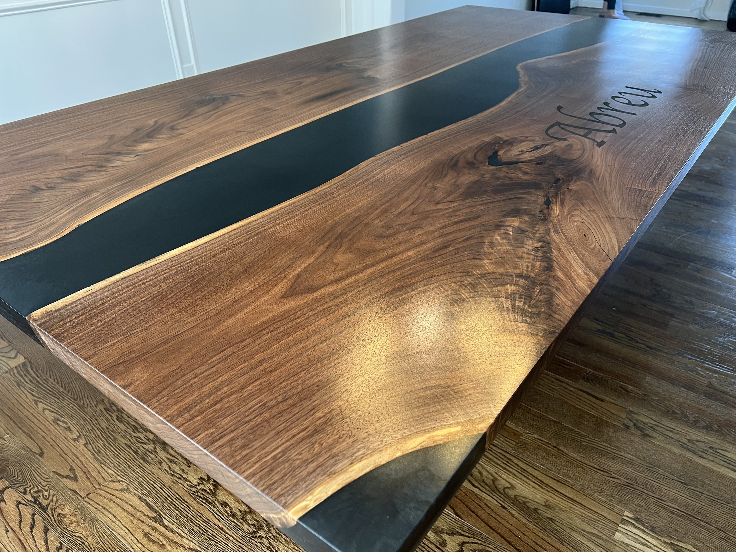 A wooden table with black epoxy inlay in the center and a partial inscription reading "YOUR NAME".