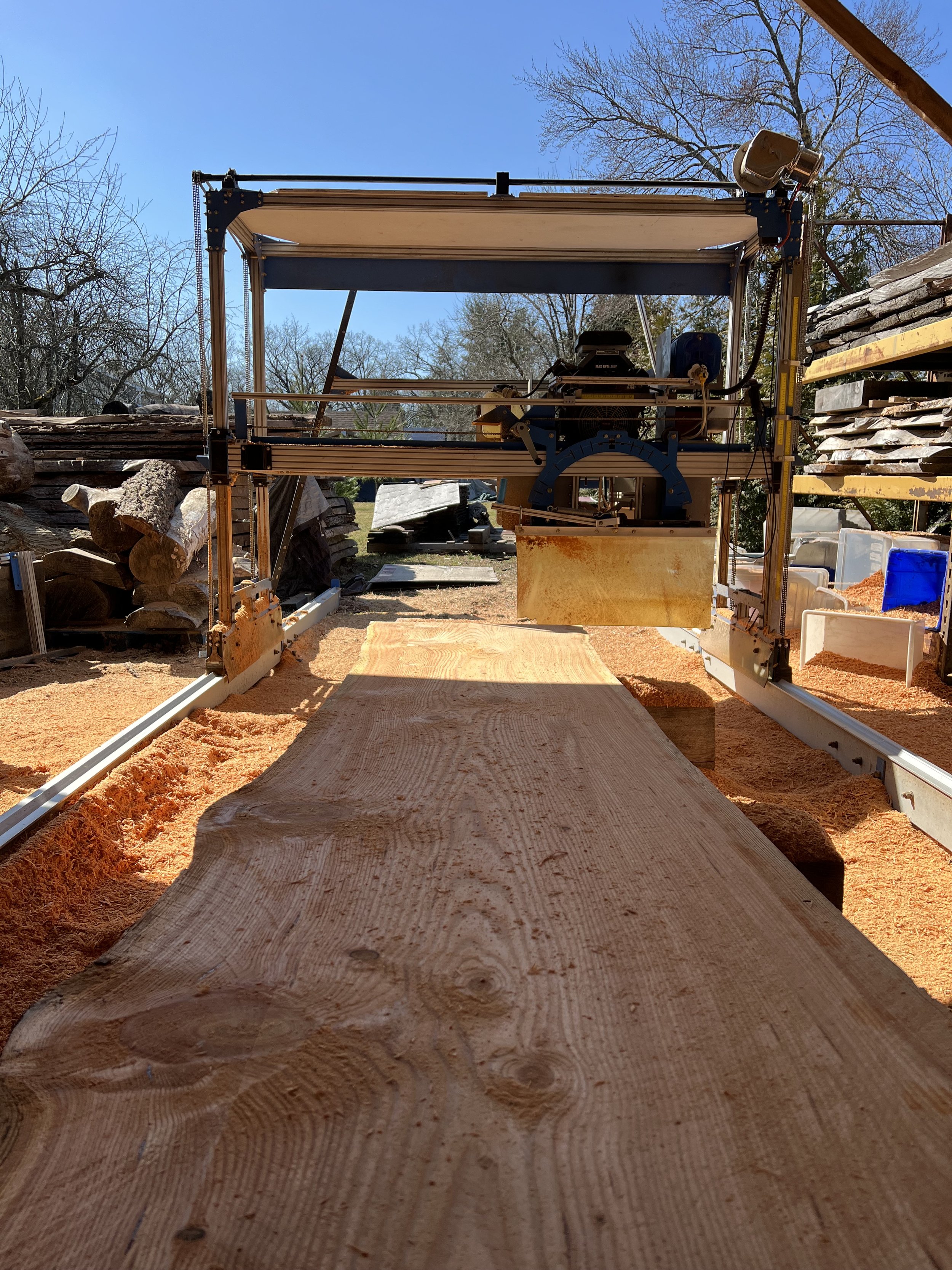 Close-up view of a sawmill or woodworking machine cutting a large wooden plank outdoors on a sunny day.