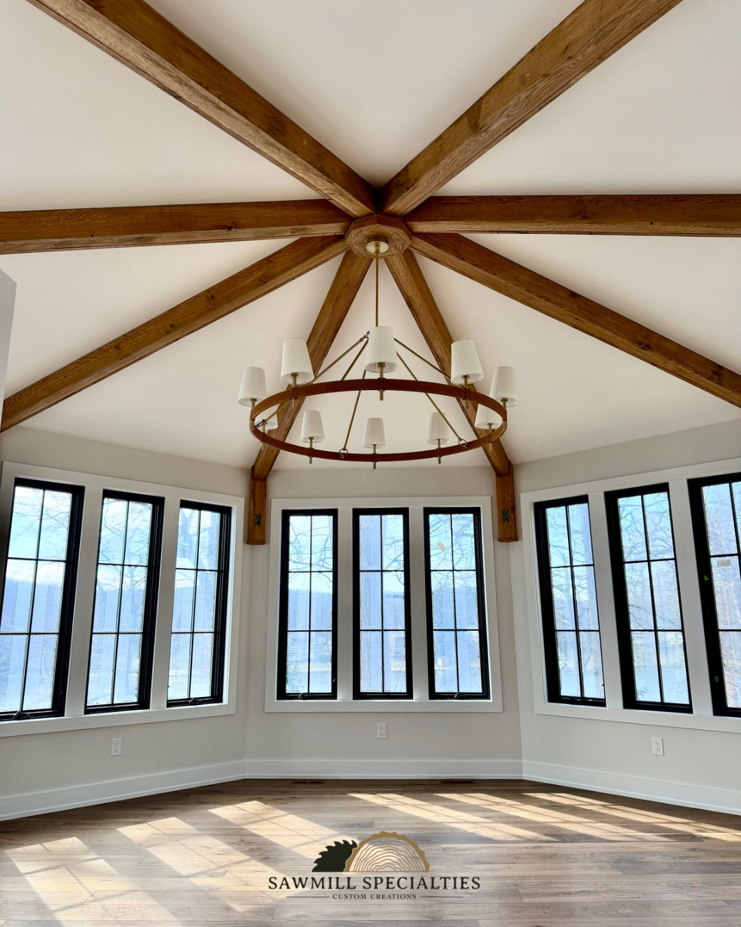 Interior view of a bright room with large windows, a wooden ceiling with exposed beams, and a chandelier with multiple white lampshades.