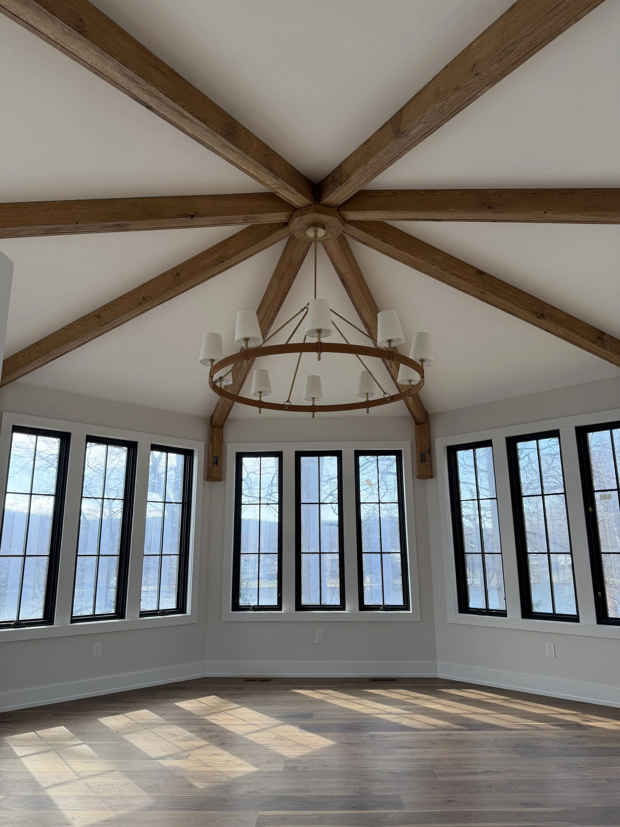 Empty room with large windows, a wooden ceiling with beams, and a circular chandelier.