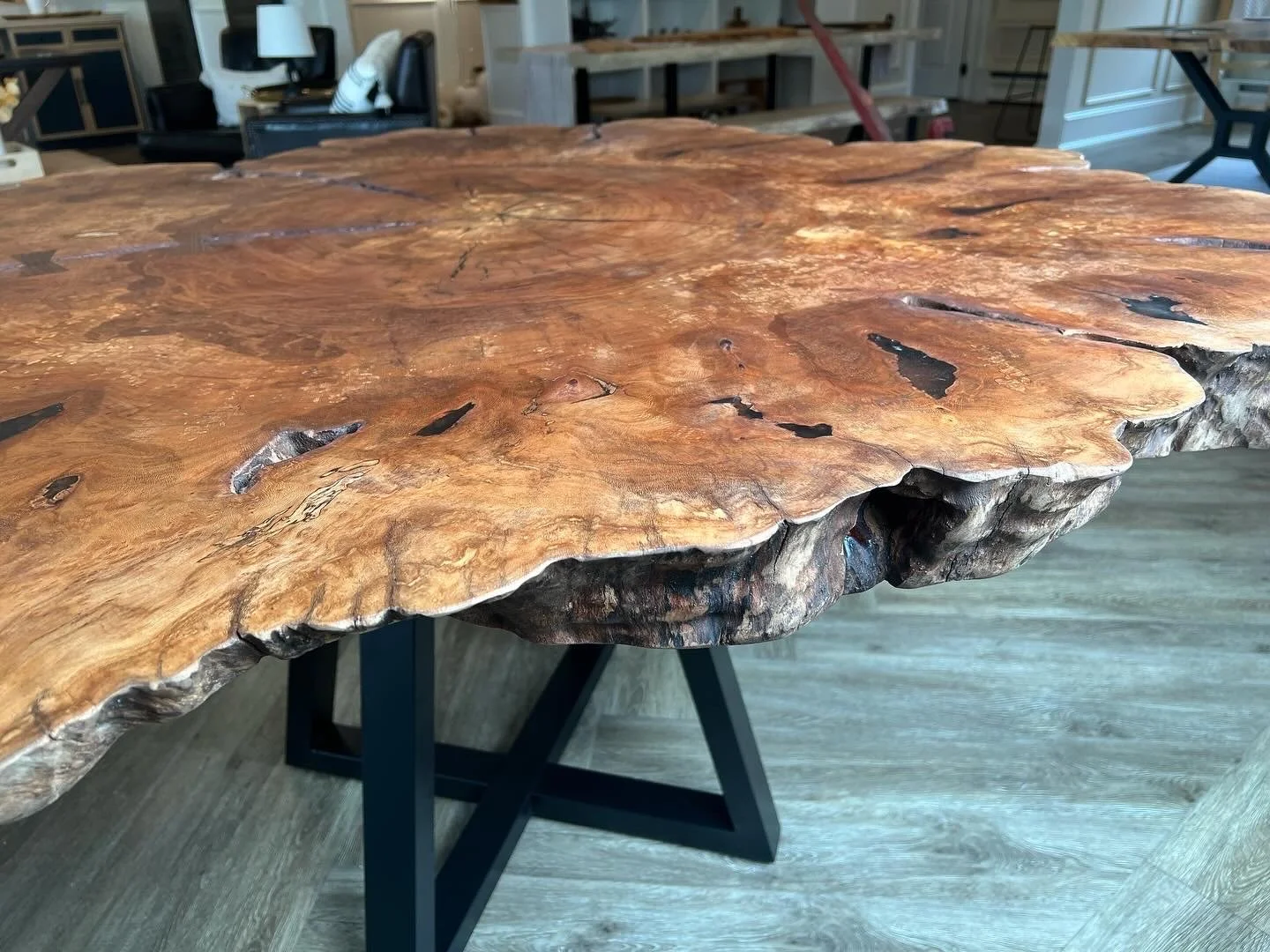 Close-up of a large, polished live-edge wood slab with natural edges and visible wood grain, supported by black metal legs.