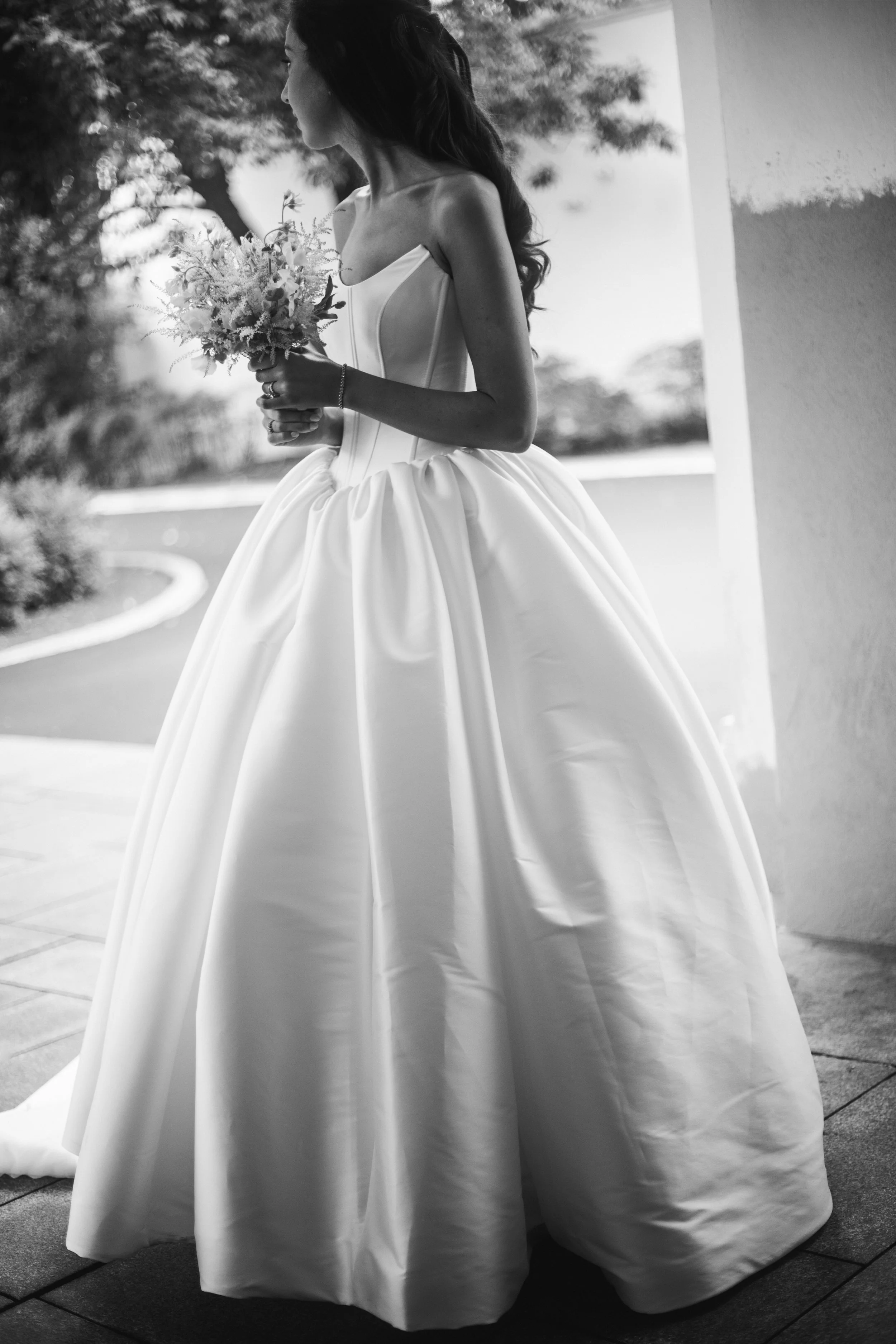 The bride stands outside at the front entrance of the country club. She is wearing a full length ballgown. Photograph taken by wedding photographer Sheridan Mangold at Congressional Country Club in Bethesda, MD.