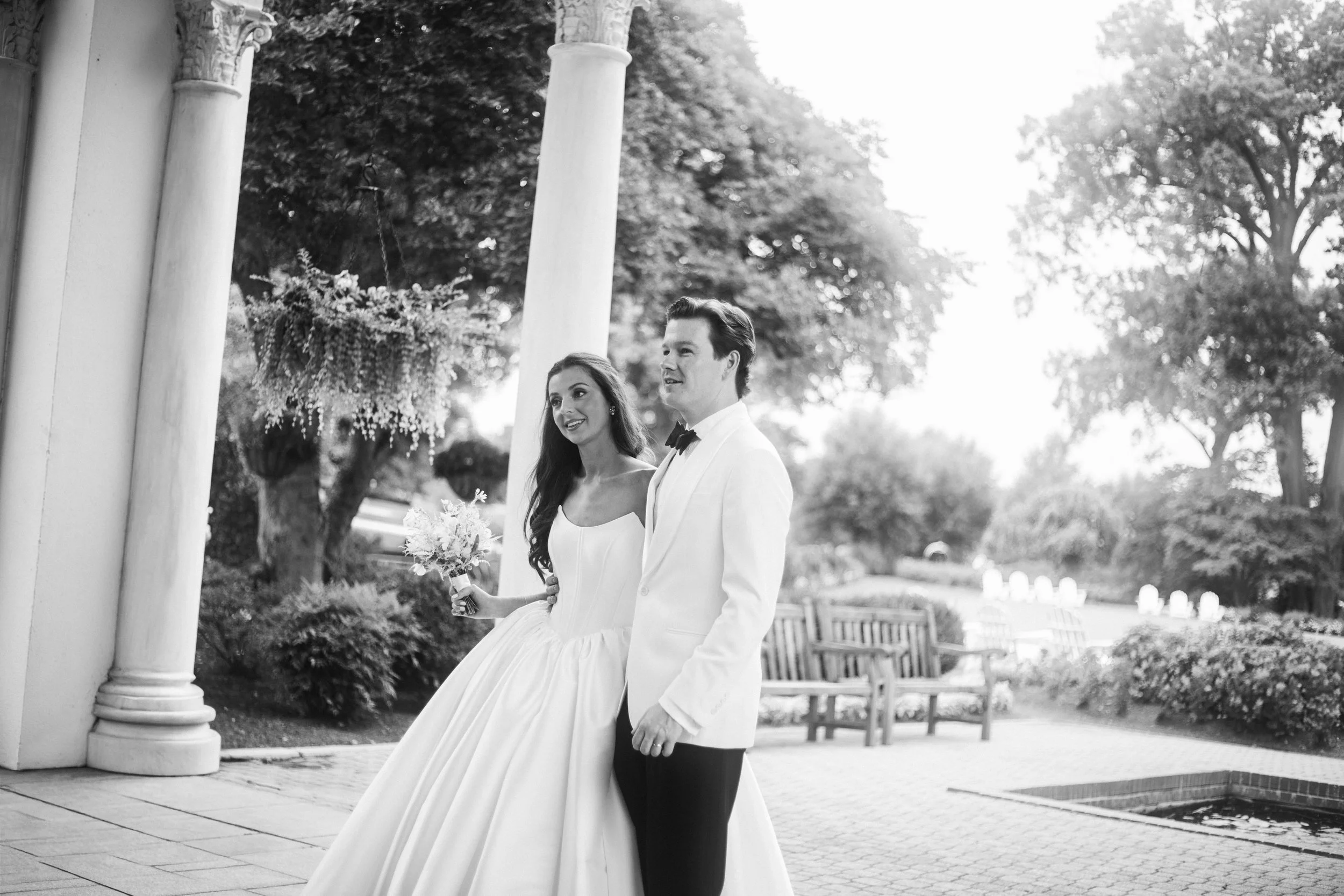 The bride stands with her groom outside of the main entrance of the club. The bride is wearing a strapless ballgown. Groom is wearing a white. Photograph taken by wedding photographer Sheridan Mangold at Congressional Country Club in Bethesda, MD.