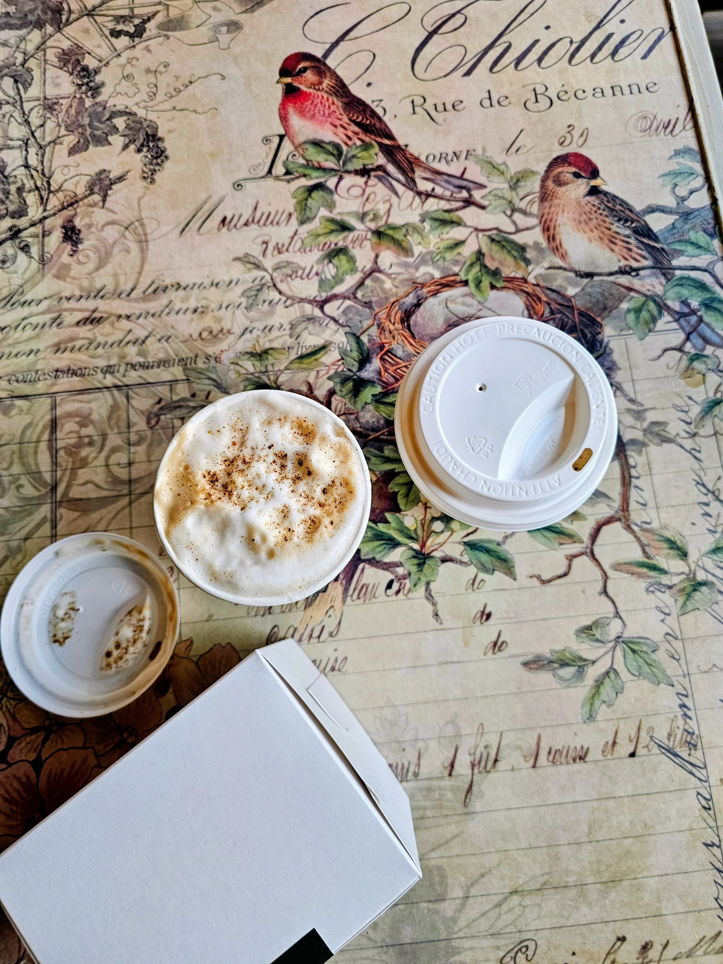 Flatlay of two lattes and a cinnamon bun in a box on a pretty table at The Ivy cafe in Sherwood Park