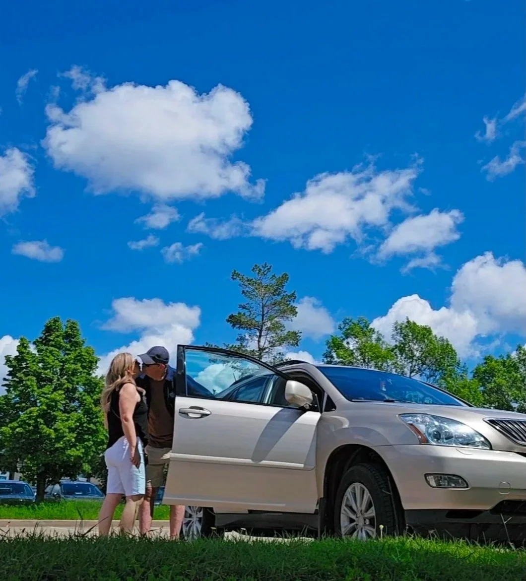 Couple sharing a kiss by their car under a bright blue sky after a spontaneous afternoon outing in Sherwood Park Alberta