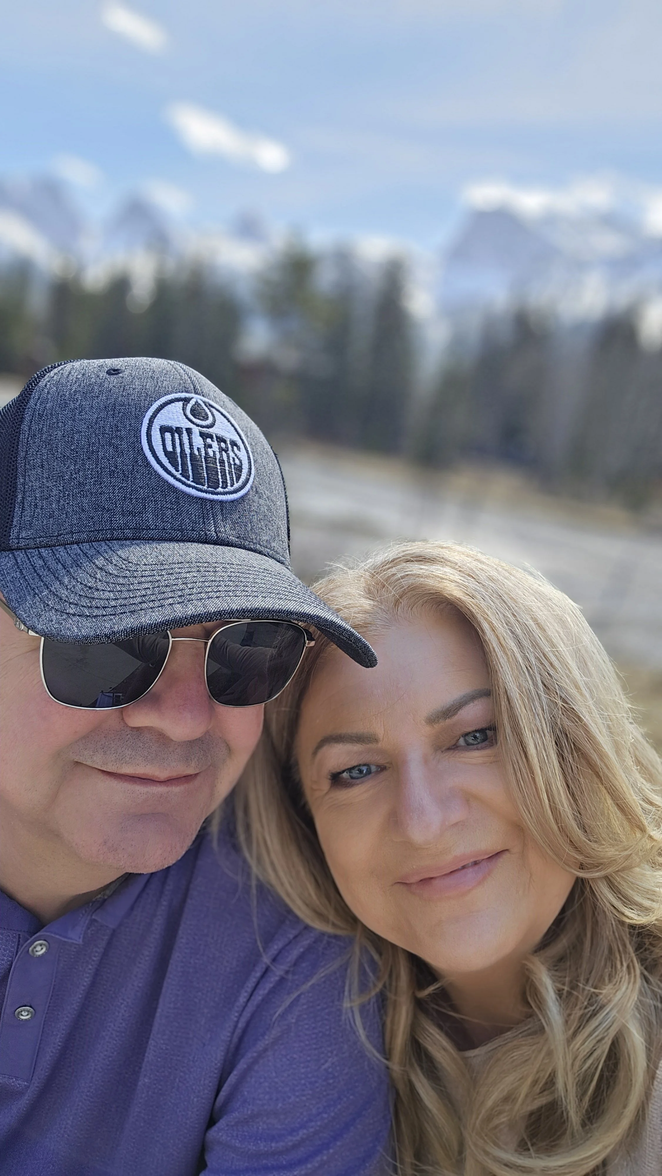 Happy GenX couple smiling together outdoors in Canmore Alberta with snow-capped Rocky Mountains in the background