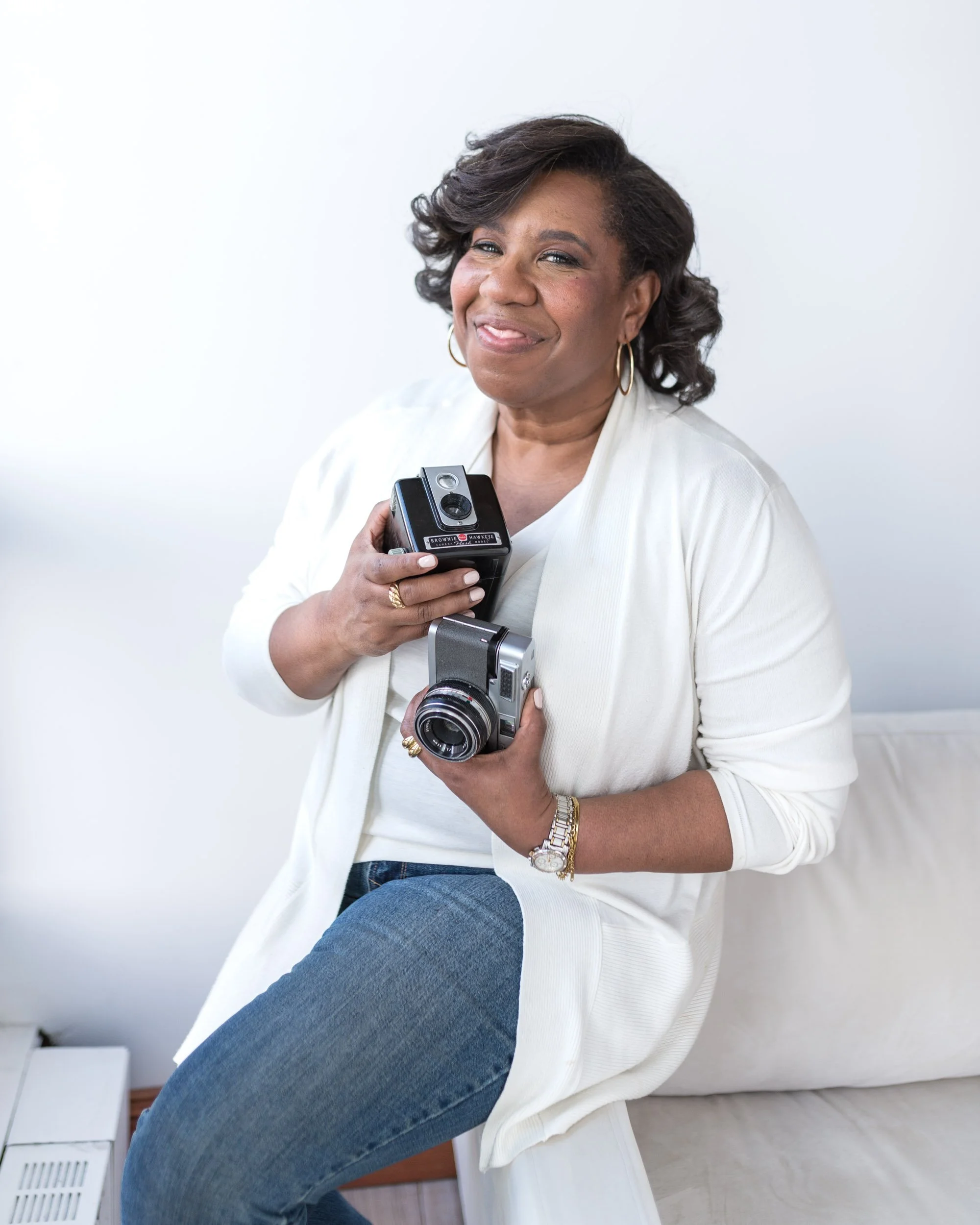 Female photographer holding cameras sitting on a sofa arm