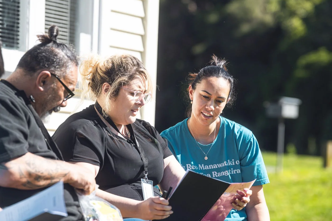 Three women sitting outdoors, looking at a notebook and talking.