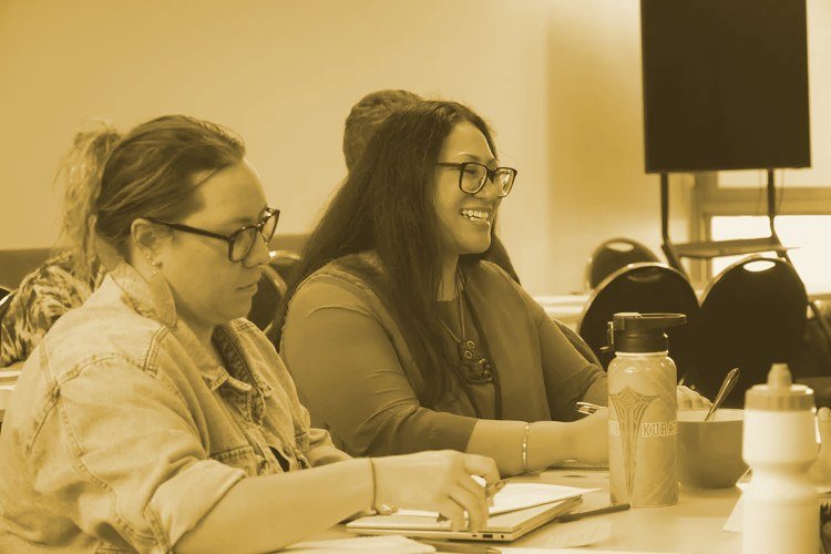 People sitting at a table in a conference room, smiling and taking notes.