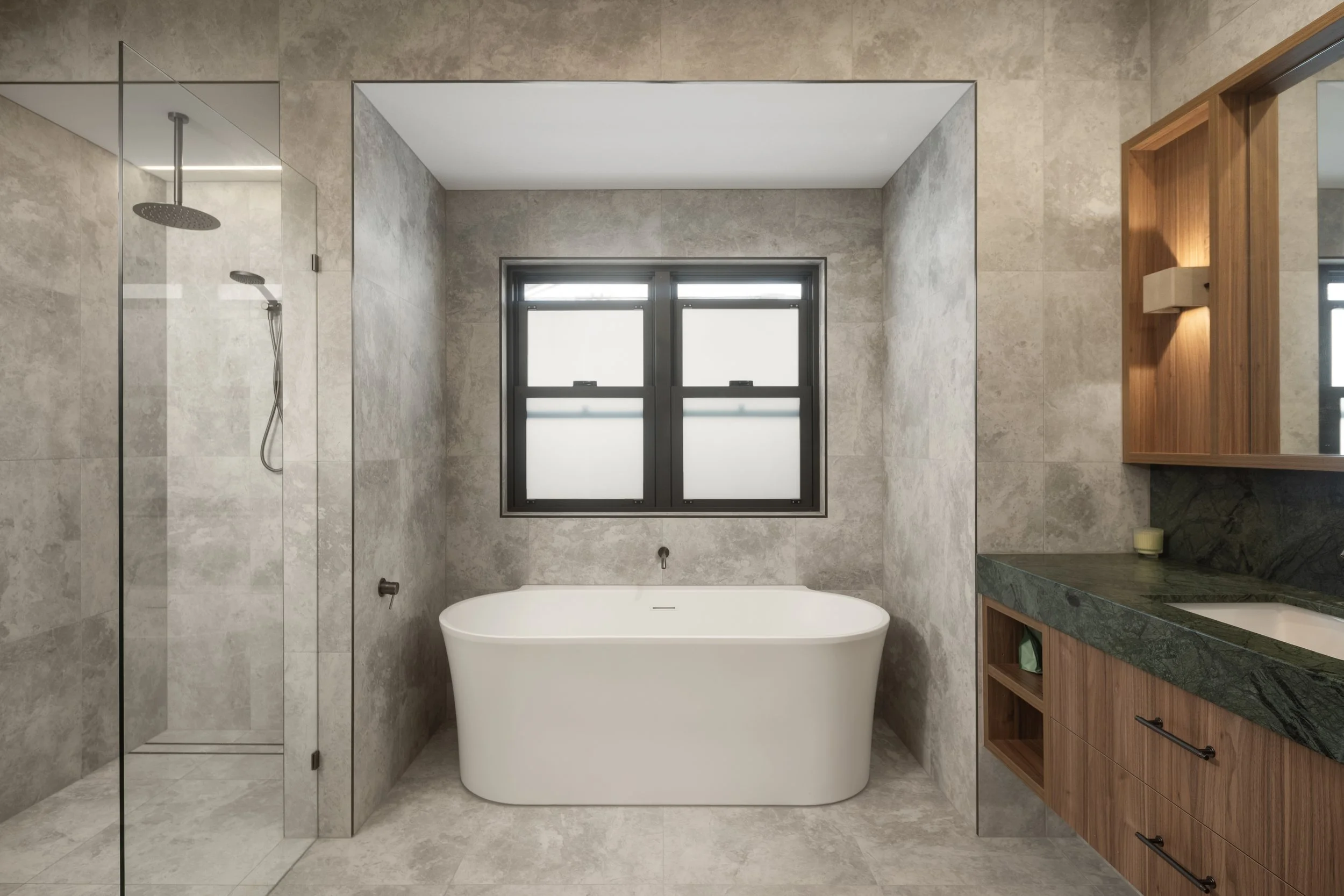 Modern bathroom with a freestanding bathtub, tiled walls, a glass-enclosed shower, and a wooden vanity with a green marble countertop.  Action Kitchens