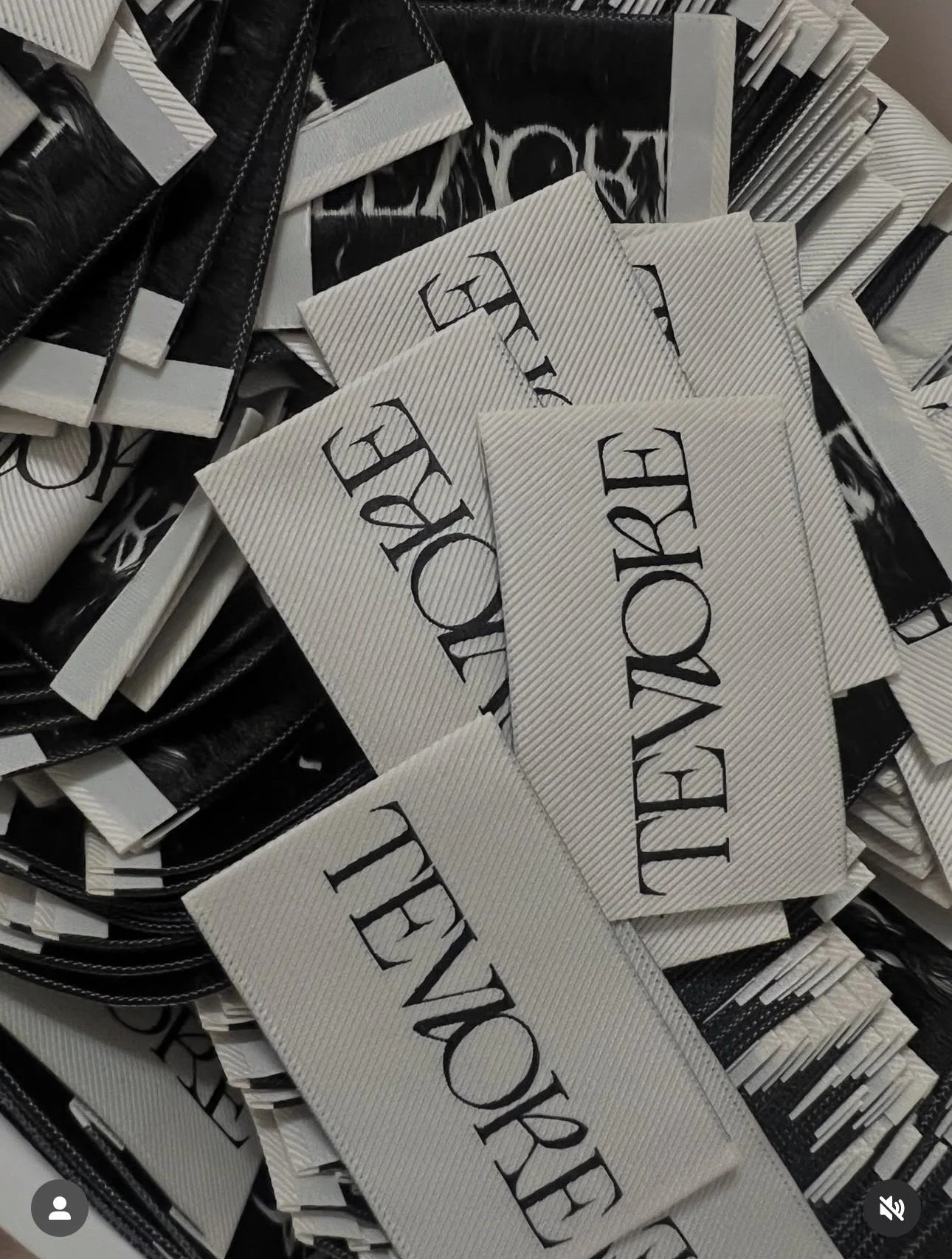 Close-up of multiple rectangular white clothing tags with the words "TEVLORE" written in black, scattered among black cards with white text, inside a container.