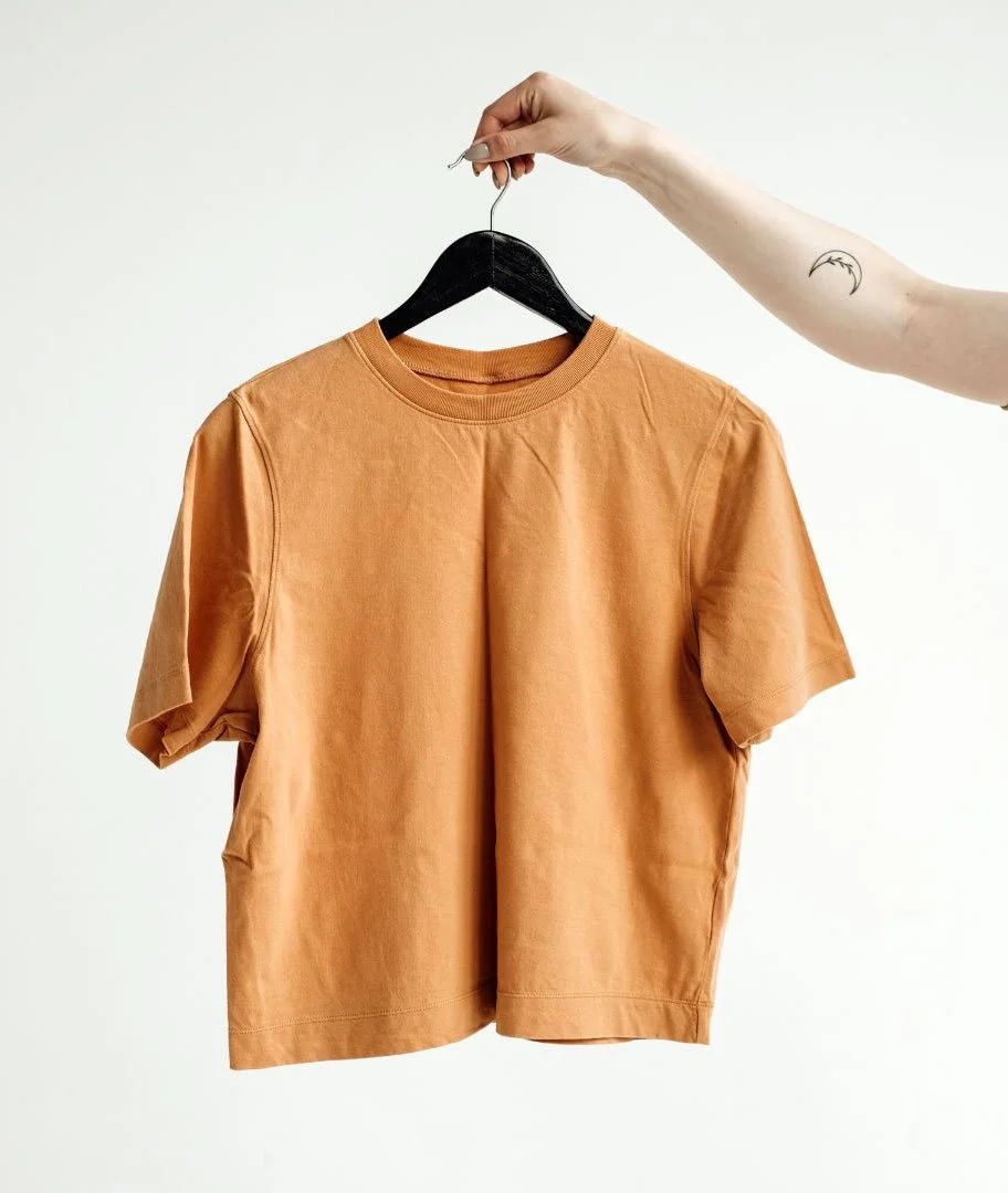 caramel colored tshirt being held up by an arm holding a black hanger