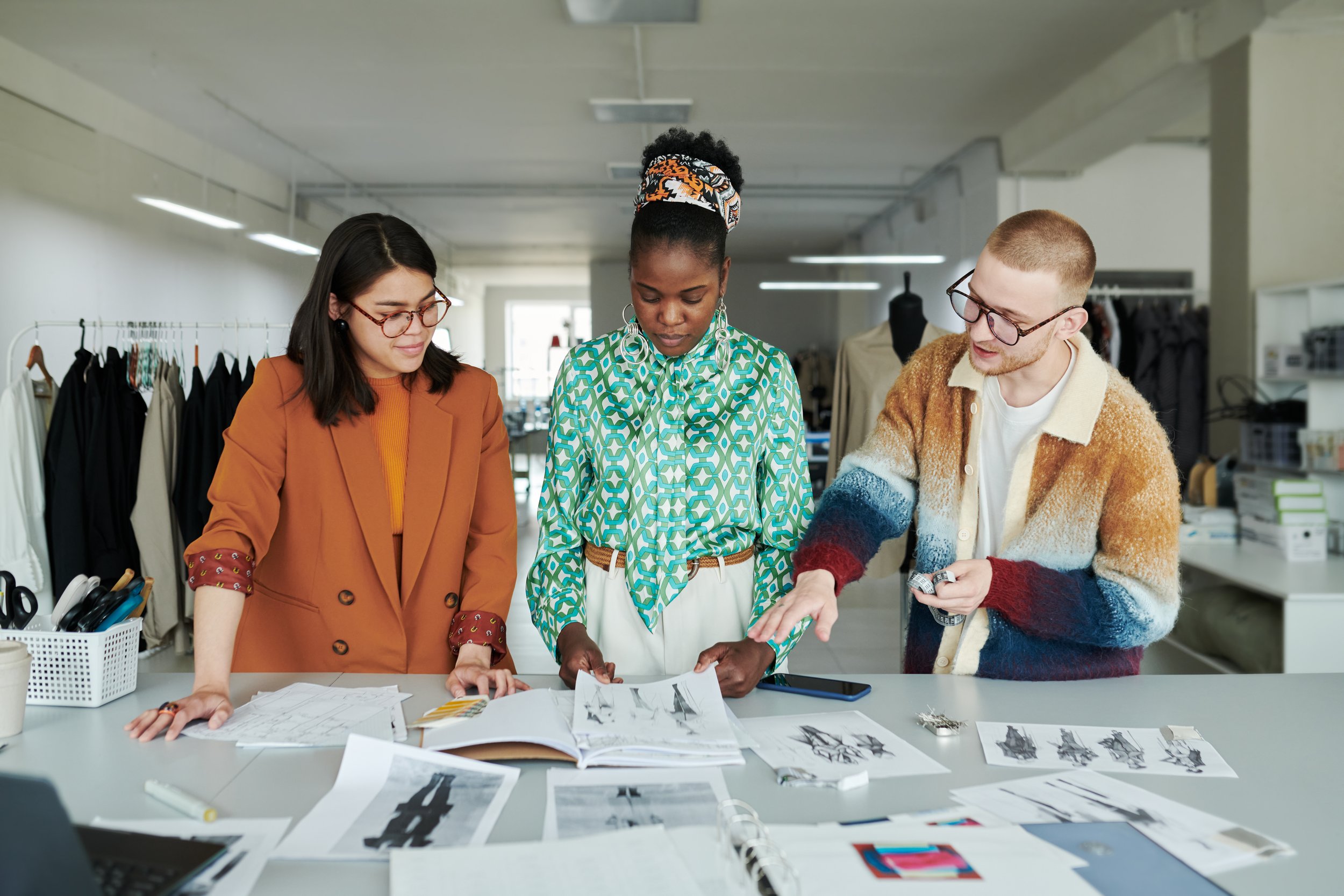 three fashion designers stand over a table reviewing sketches