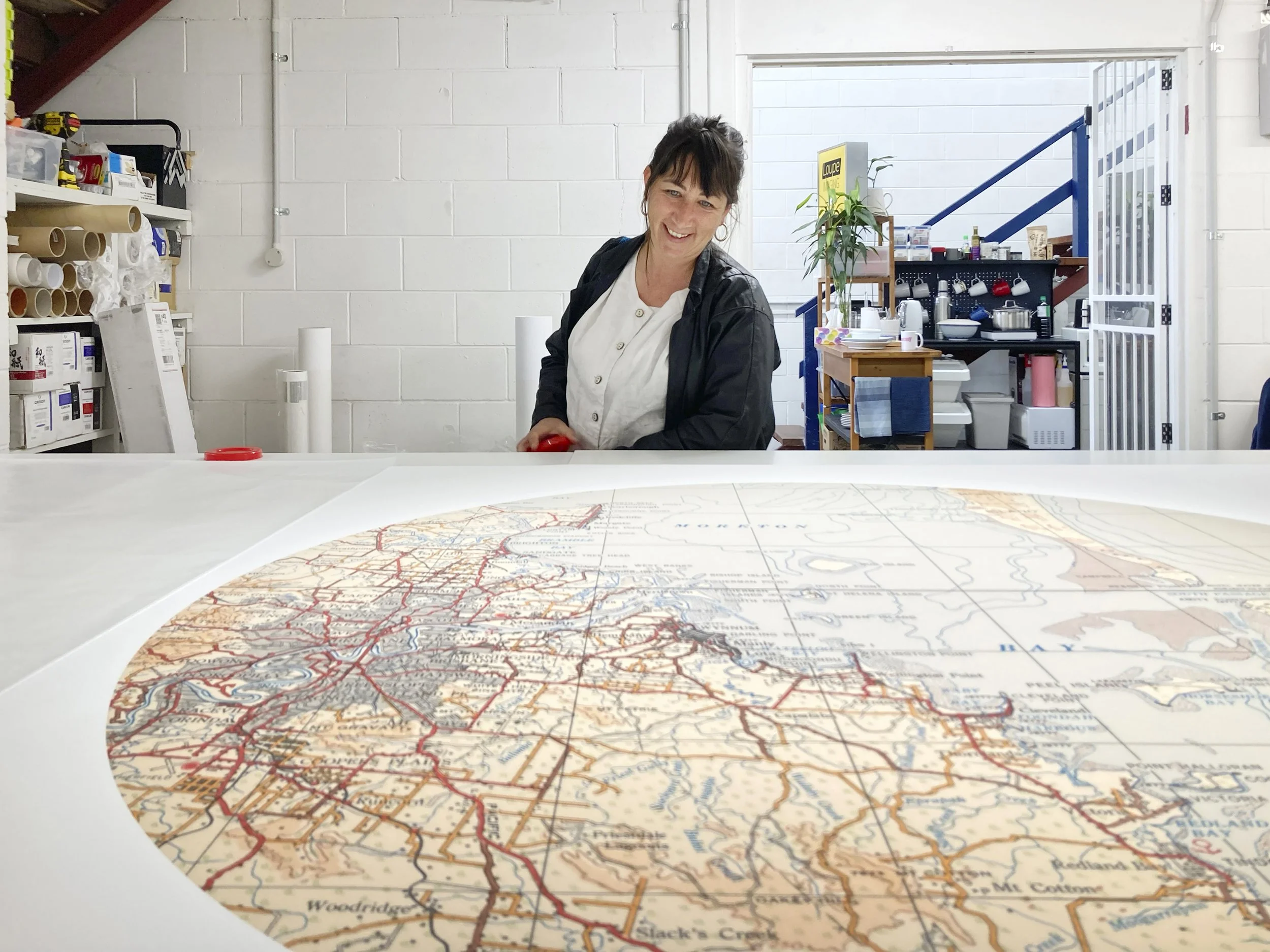 Artist Megan Cope smiling at a large colour map print for her artwork on a table