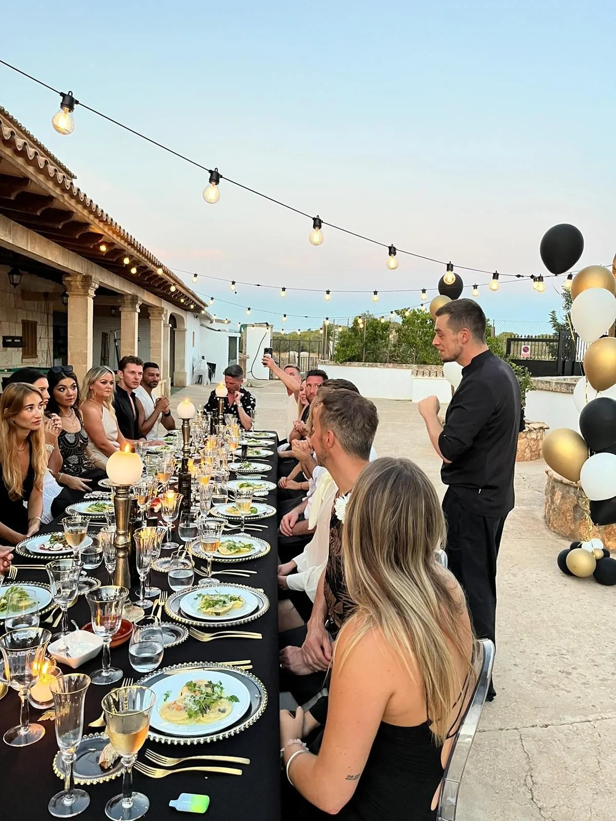 Guests seated at a navy and gold celebration dinner on a Mallorca villa terrace at dusk