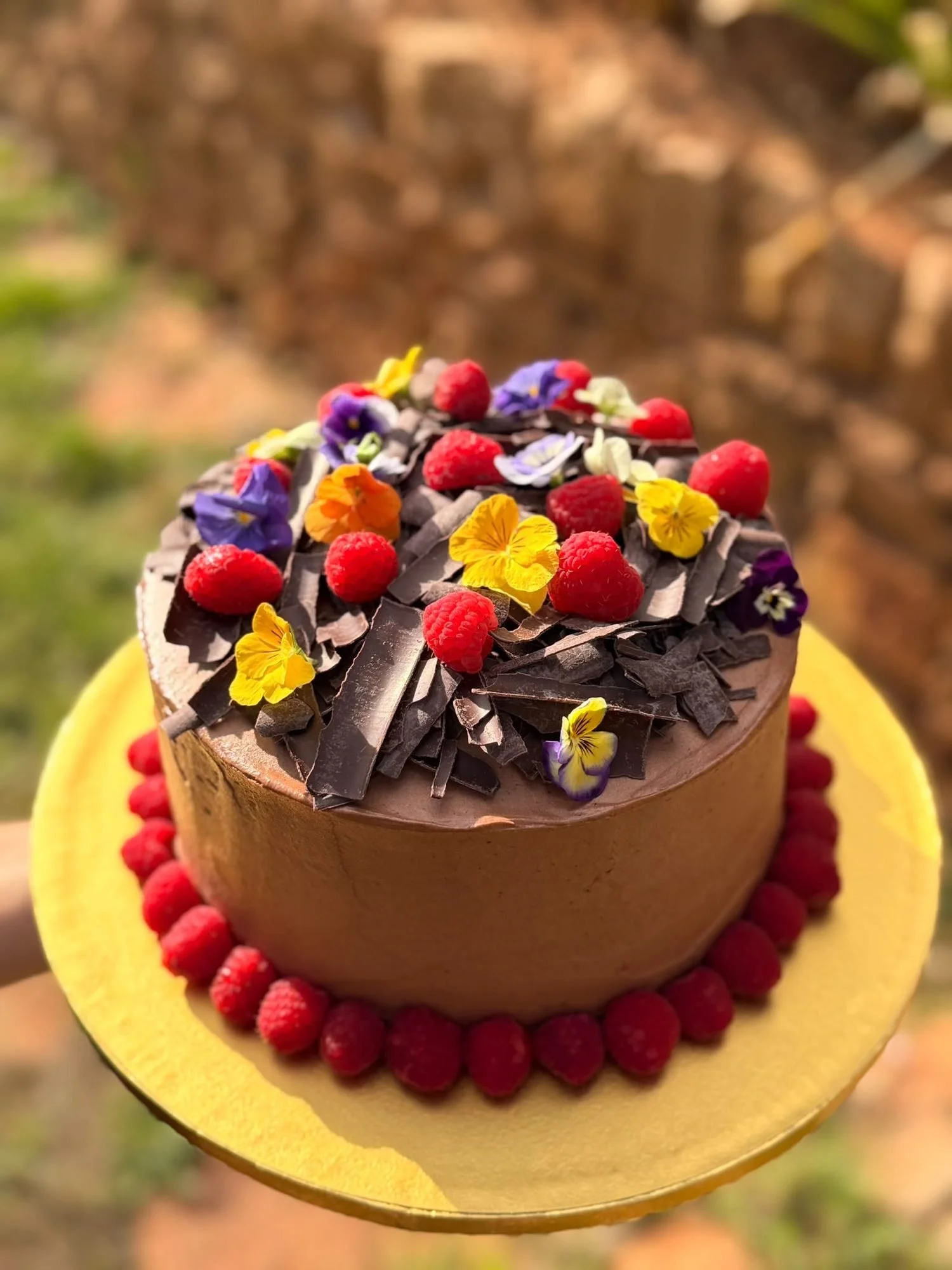 Chocolate celebration cake topped with edible flowers and raspberries, made for a party in Mallorca