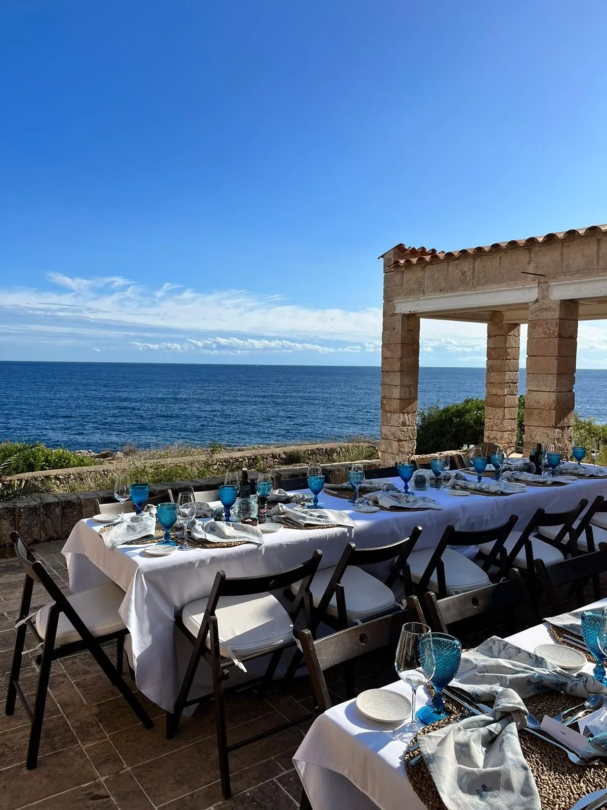 Long white-linen table set for a celebration on a clifftop terrace above the sea in Mallorca