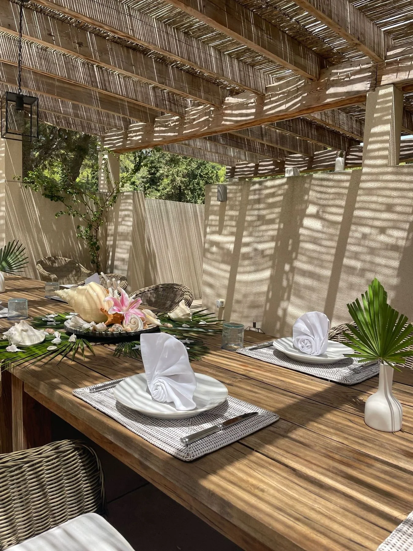 Pergola dining table with white plates, folded napkins and fresh flowers, set by Bluelime Bespoke in Mallorca