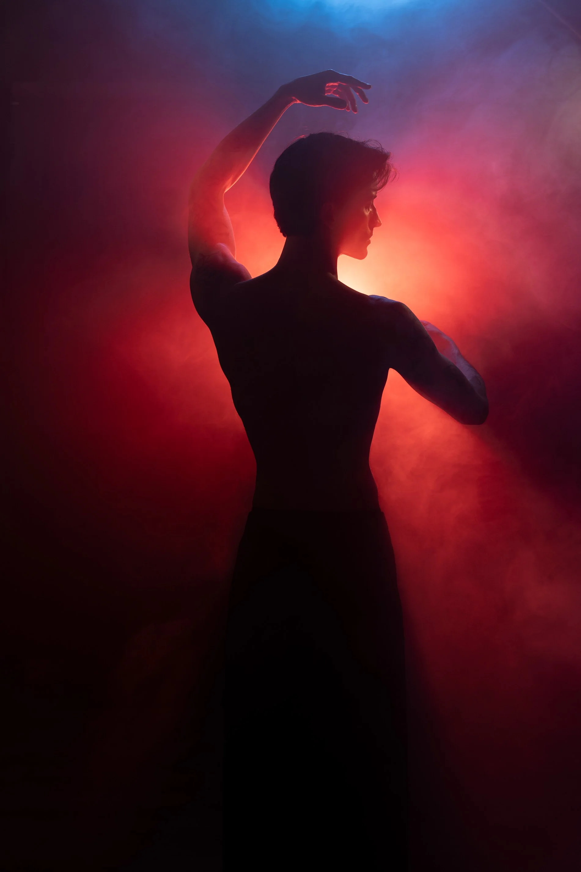 Schatten eines männlichen Tänzers vor einer bunten, neonartigen Hintergrundbeleuchtung, der eine elegante Pose einnimmt.