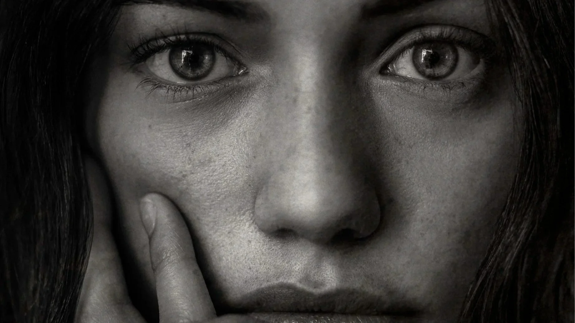 Nahaufnahme eines menschlichen Gesichts in schwarz-weiß, mit einem Blick in die Kamera, eine Hand berührt das Kinn.