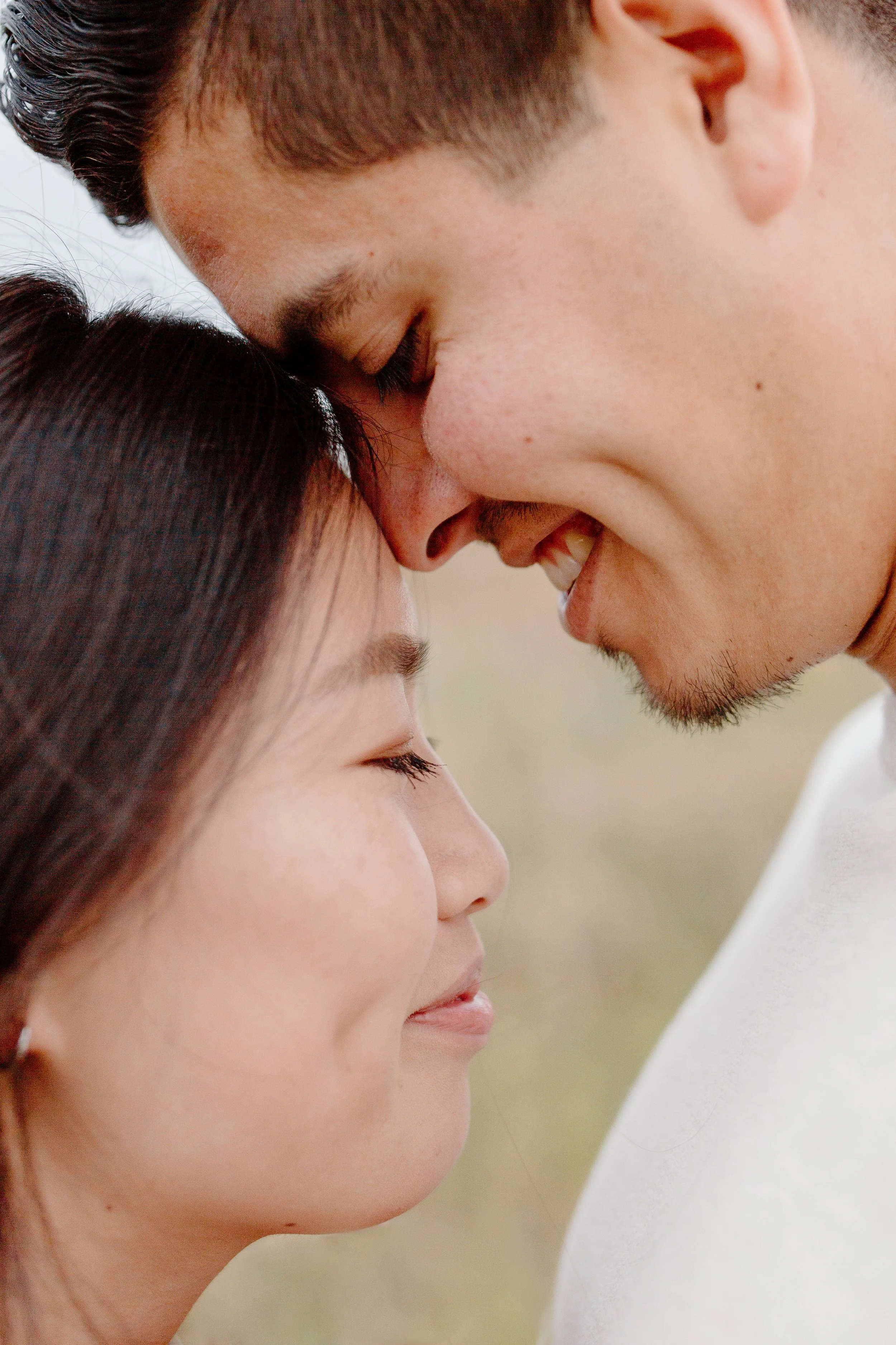 A close-up of a couple touching foreheads and smiling with eyes closed, outdoors.