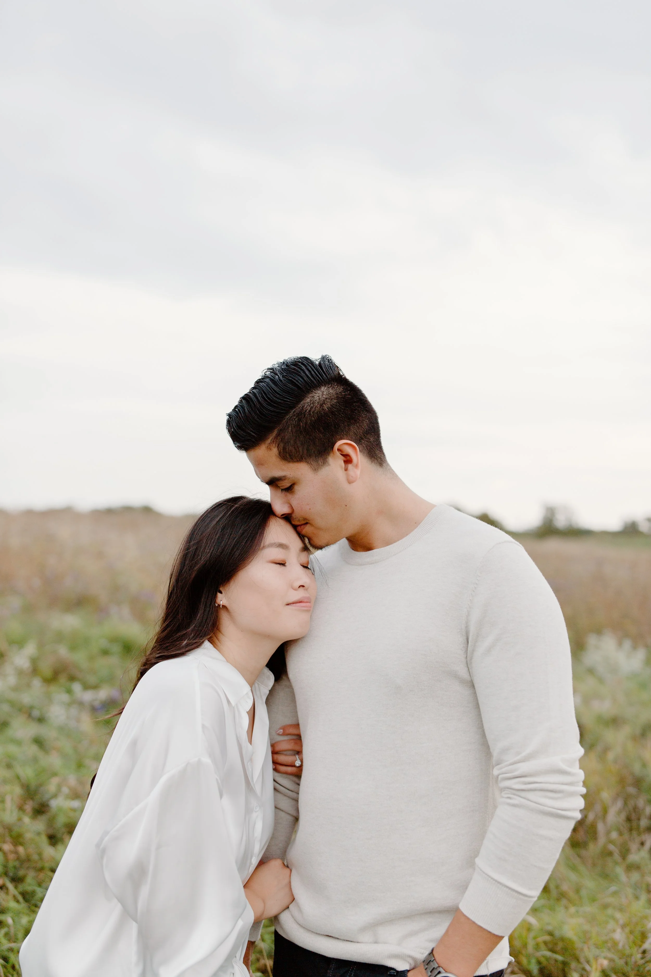 A couple sharing a tender moment outdoors with the man kissing the woman's forehead.