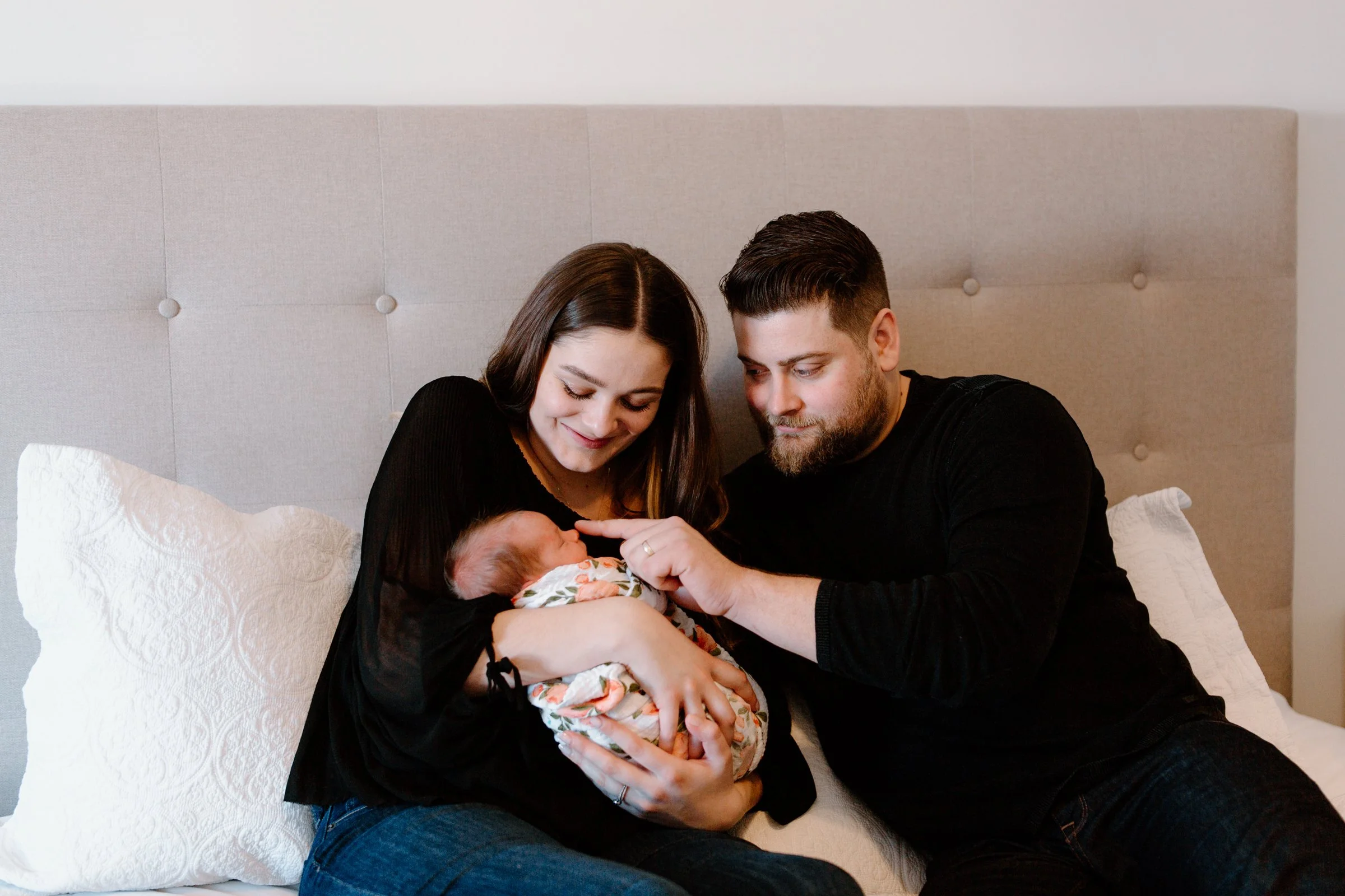 A couple holding a newborn baby on a bed, looking at the baby affectionately.