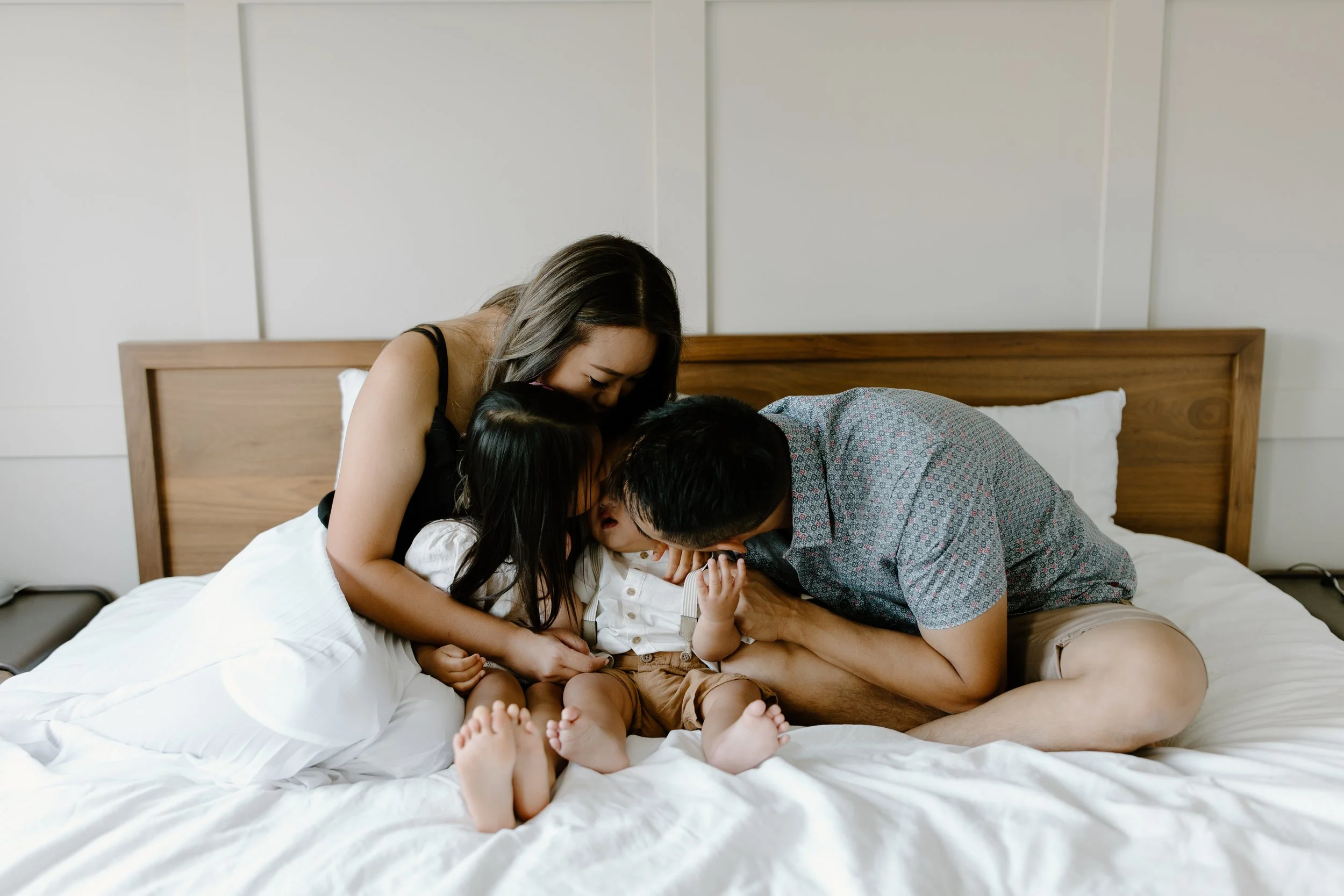 A family of three, a woman, man, and a young boy, are cuddling together on a bed, with their faces close and eyes closed.