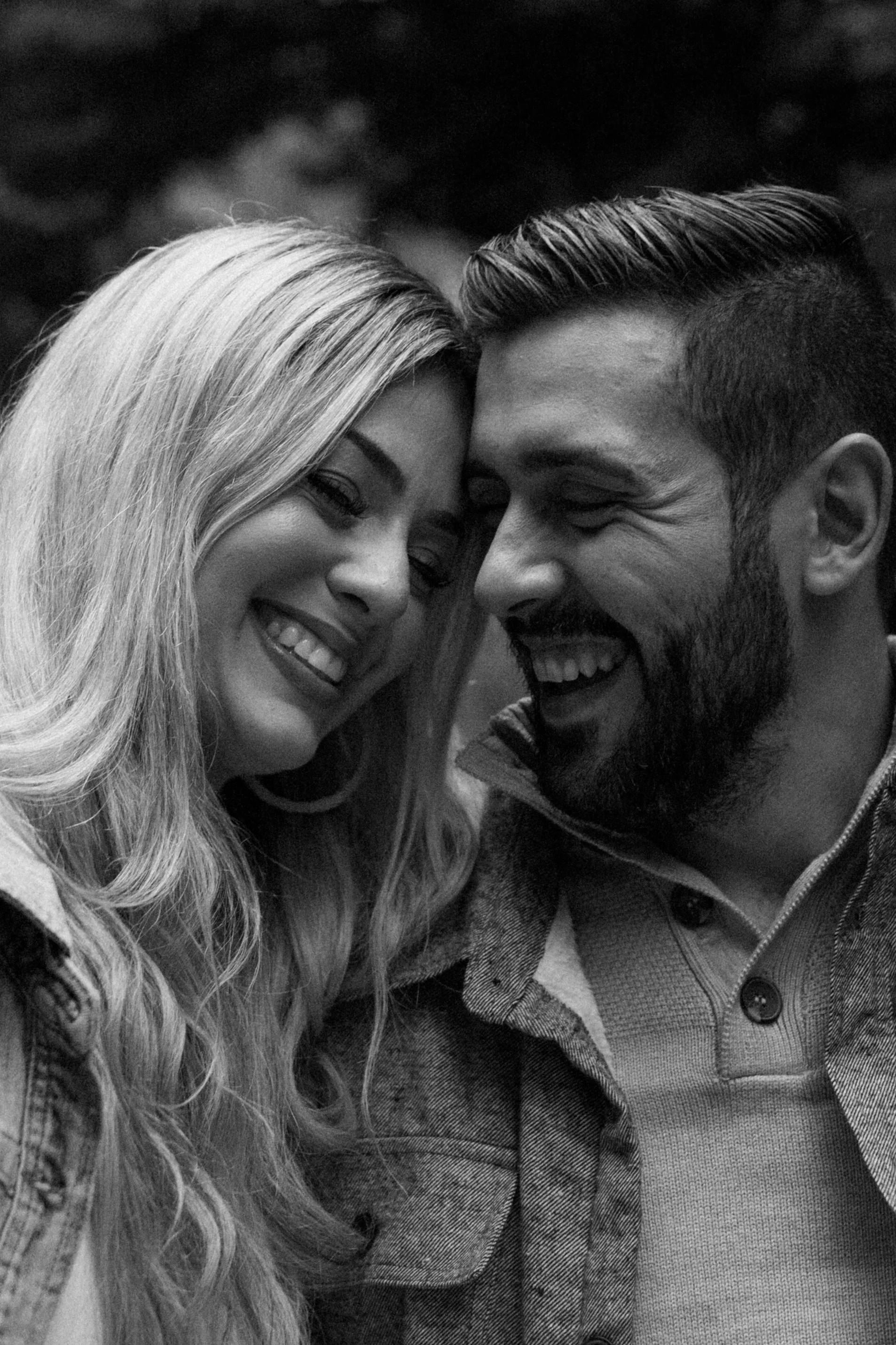 A black and white photo of a smiling couple with their foreheads touching, showing their happiness.