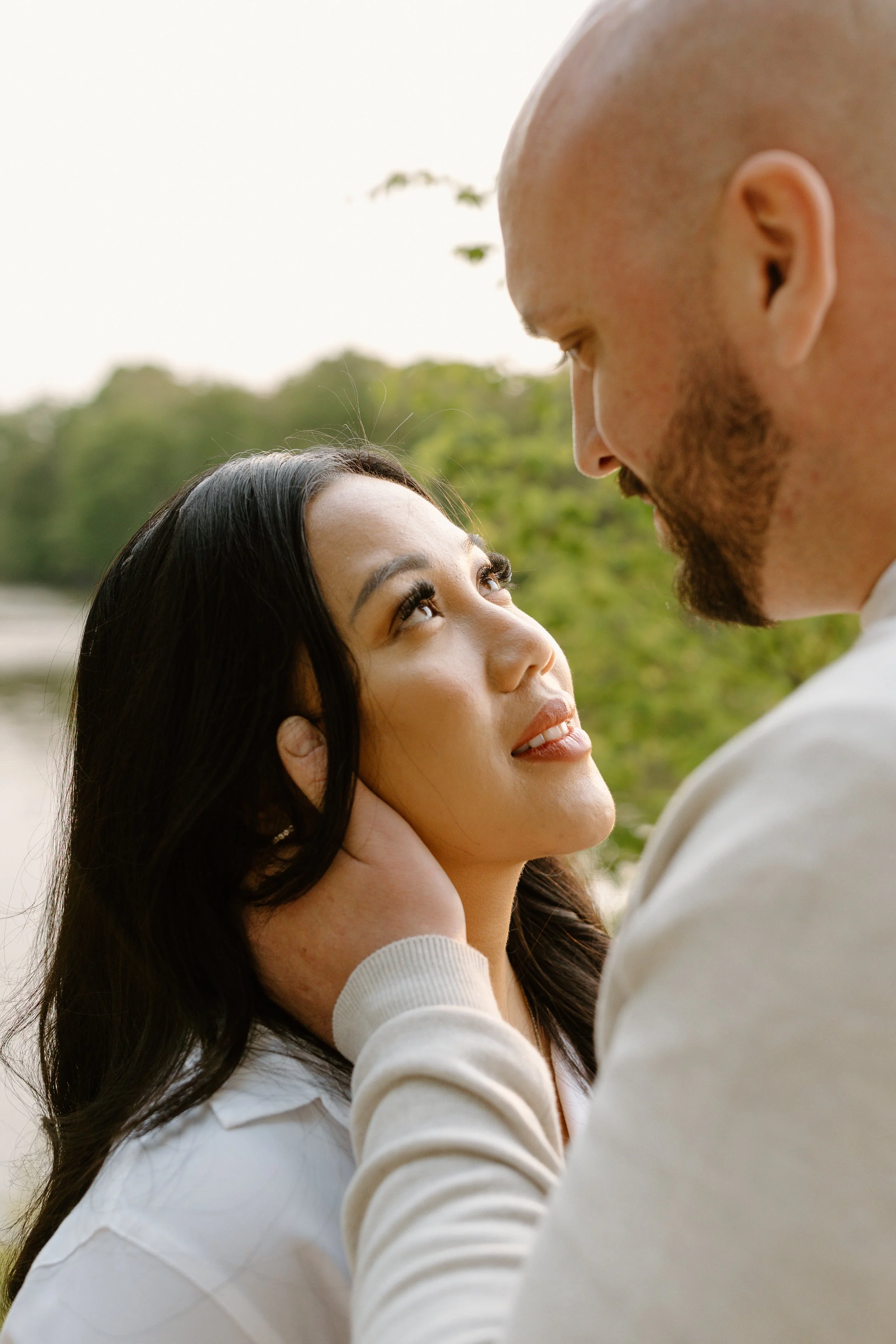 A couple gazing into each other's eyes outdoors with greenery in the background.