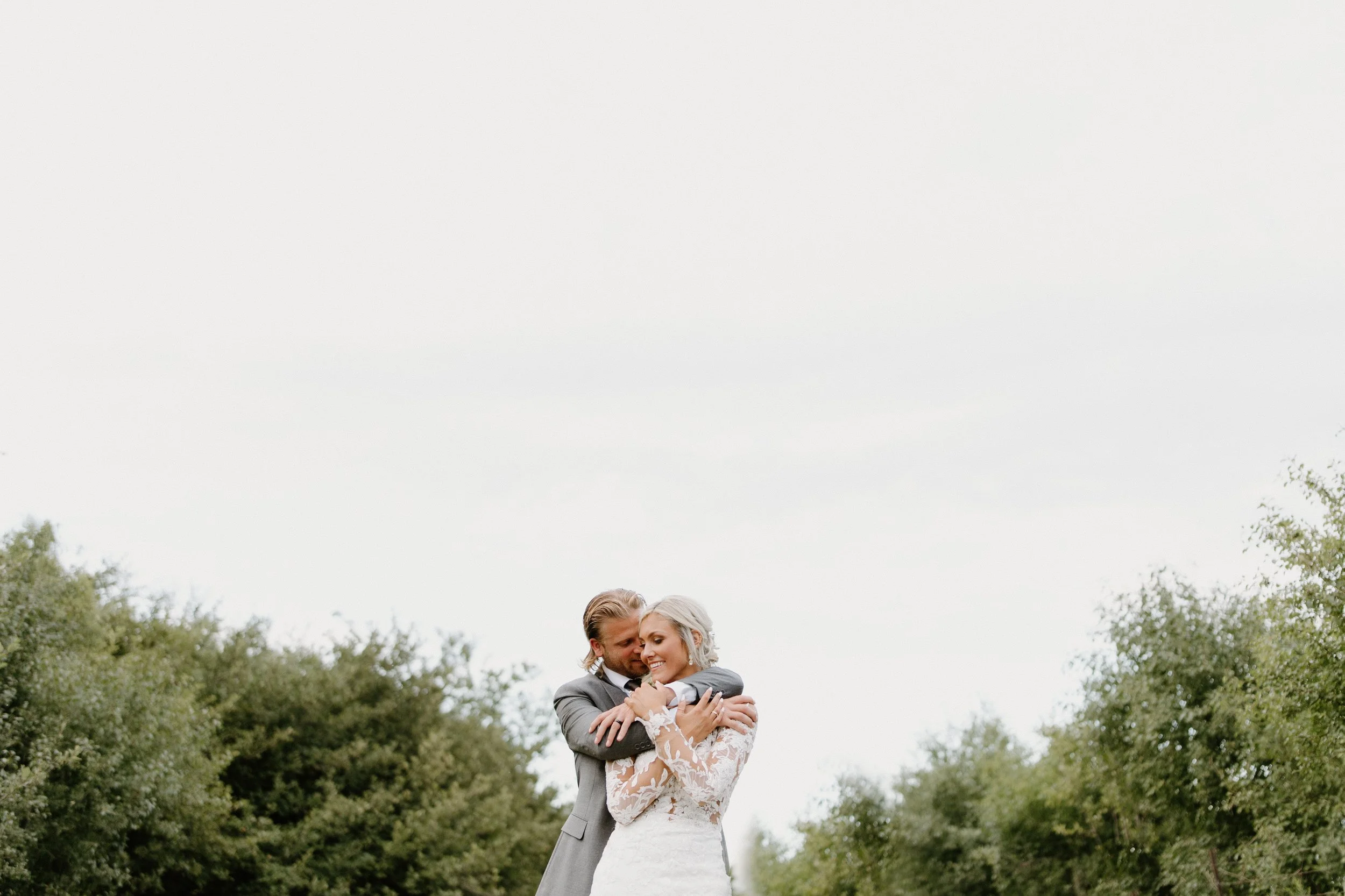 Bride and groom embracing outdoors in a natural setting with trees in the background.