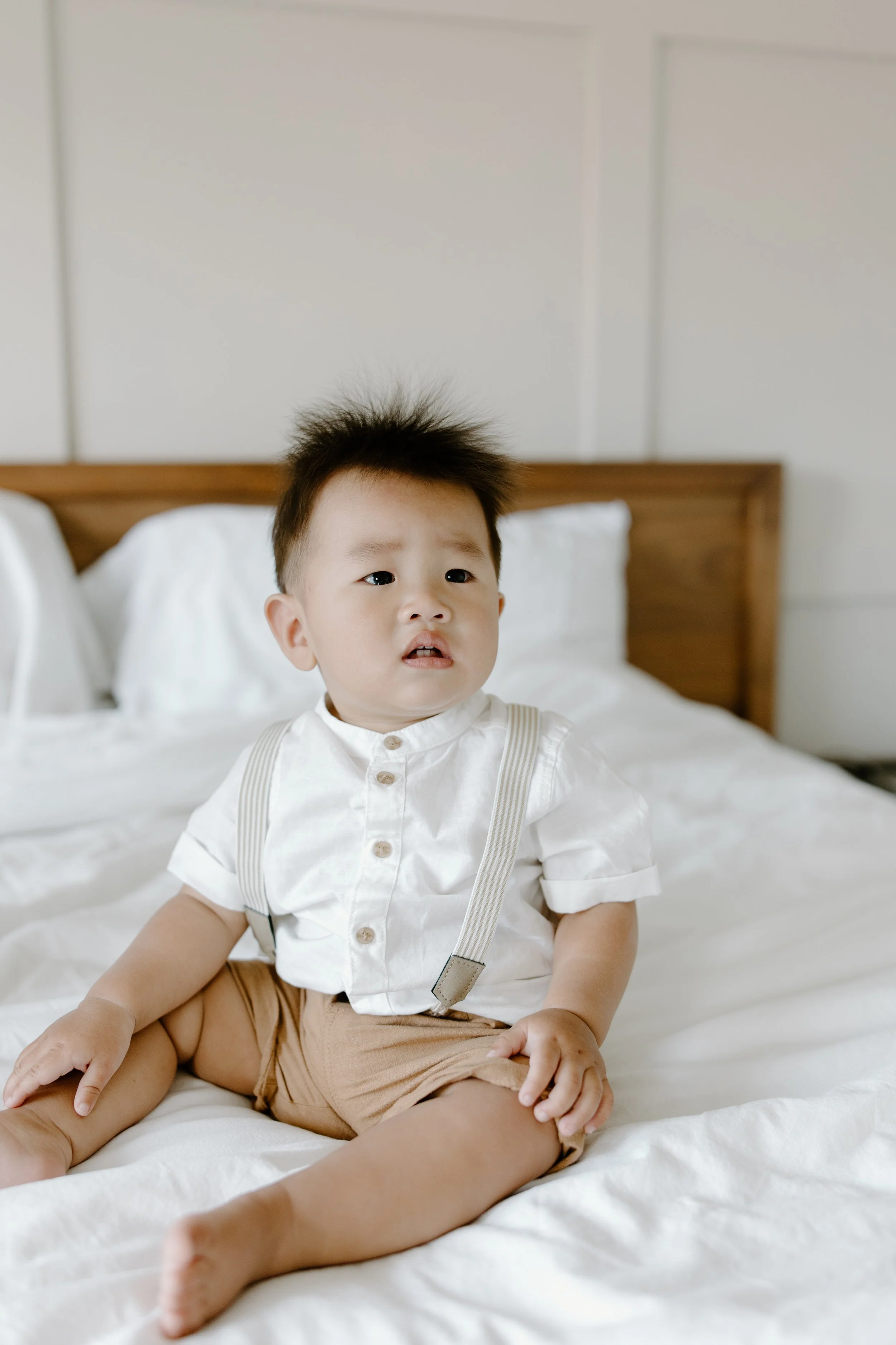 A young child sitting on a bed, looking confused or upset.