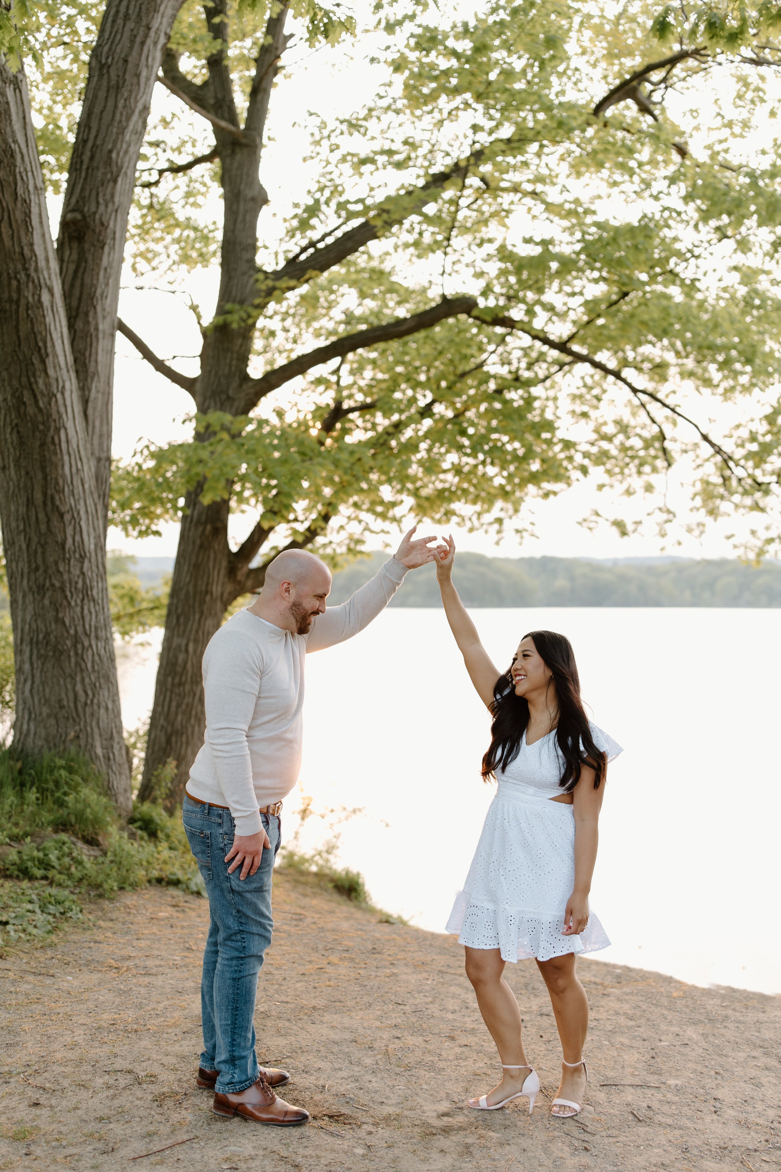 A couple dancing outdoors by a lake, with trees and water in the background, during what appears to be late afternoon or early evening.