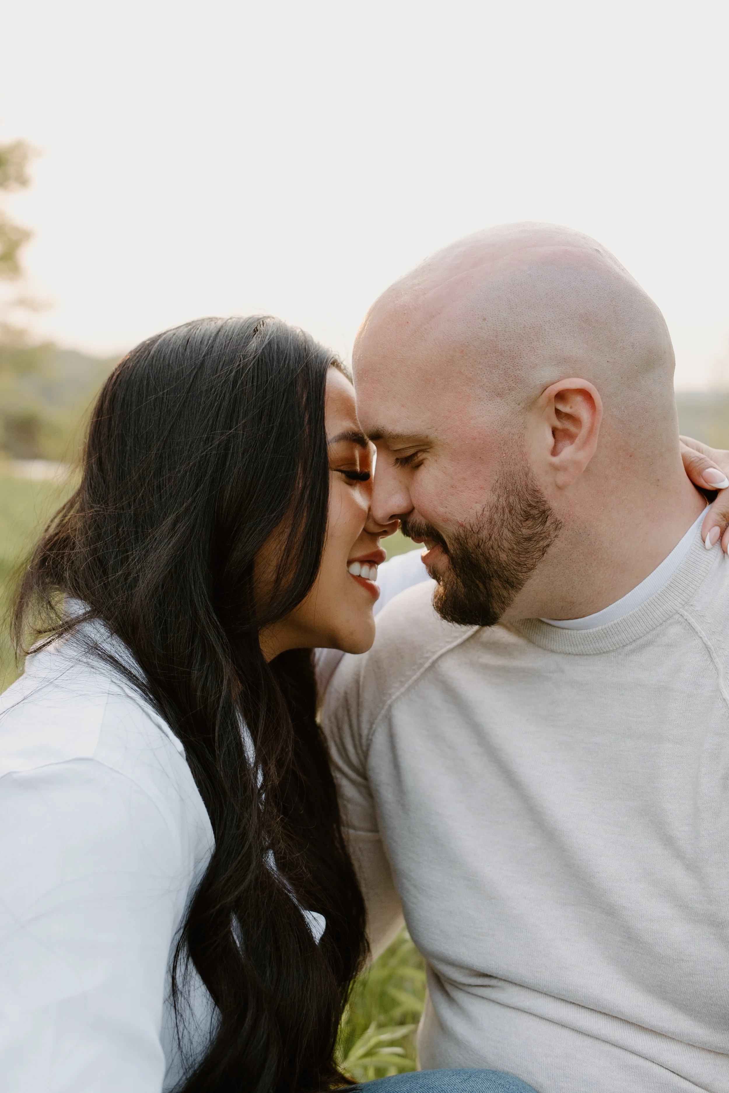 A couple with closed eyes and smiling faces touching foreheads outdoors in a natural setting.