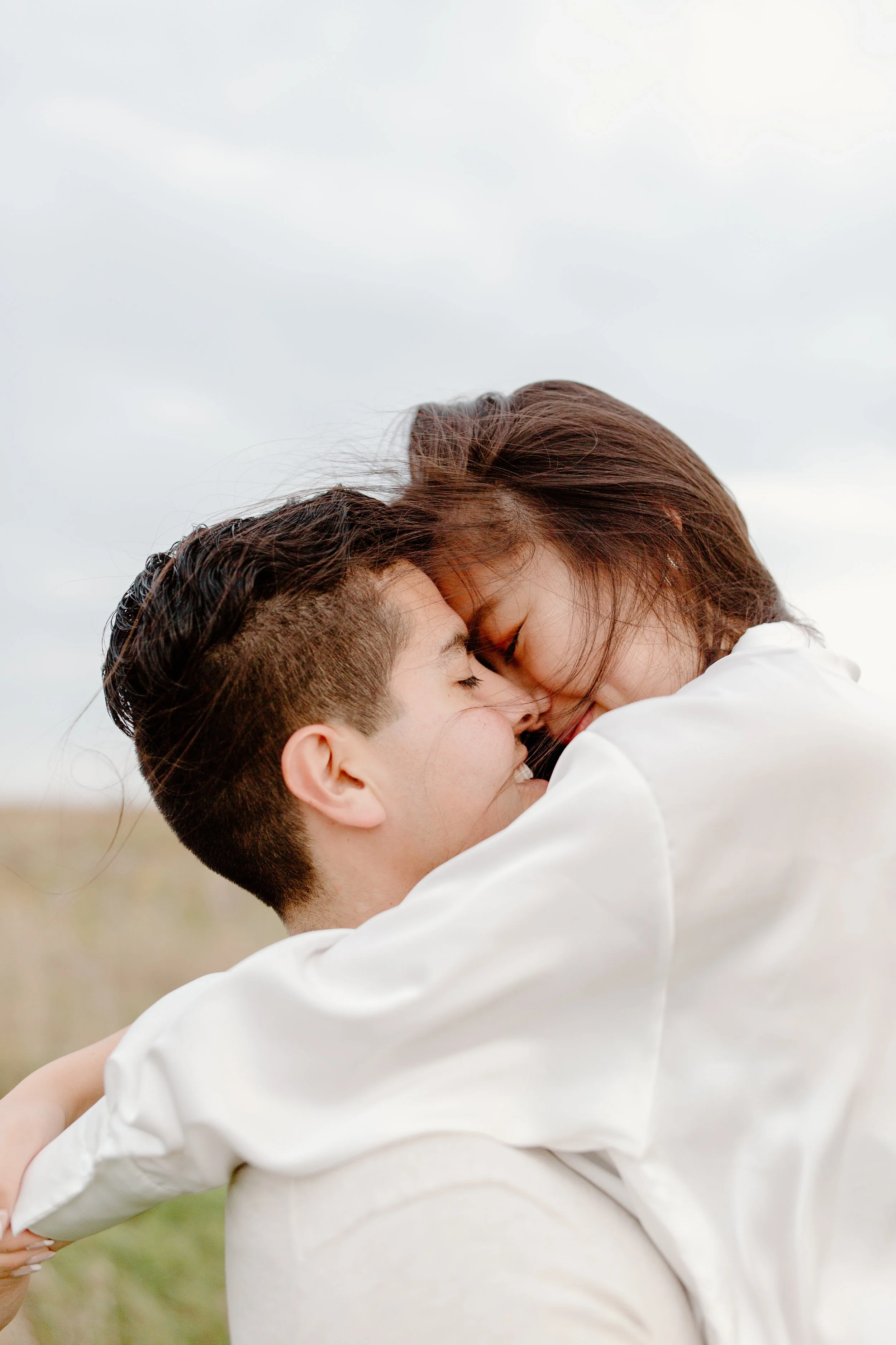 Two women embracing and touching foreheads with closed eyes, smiling gently in an outdoor setting.