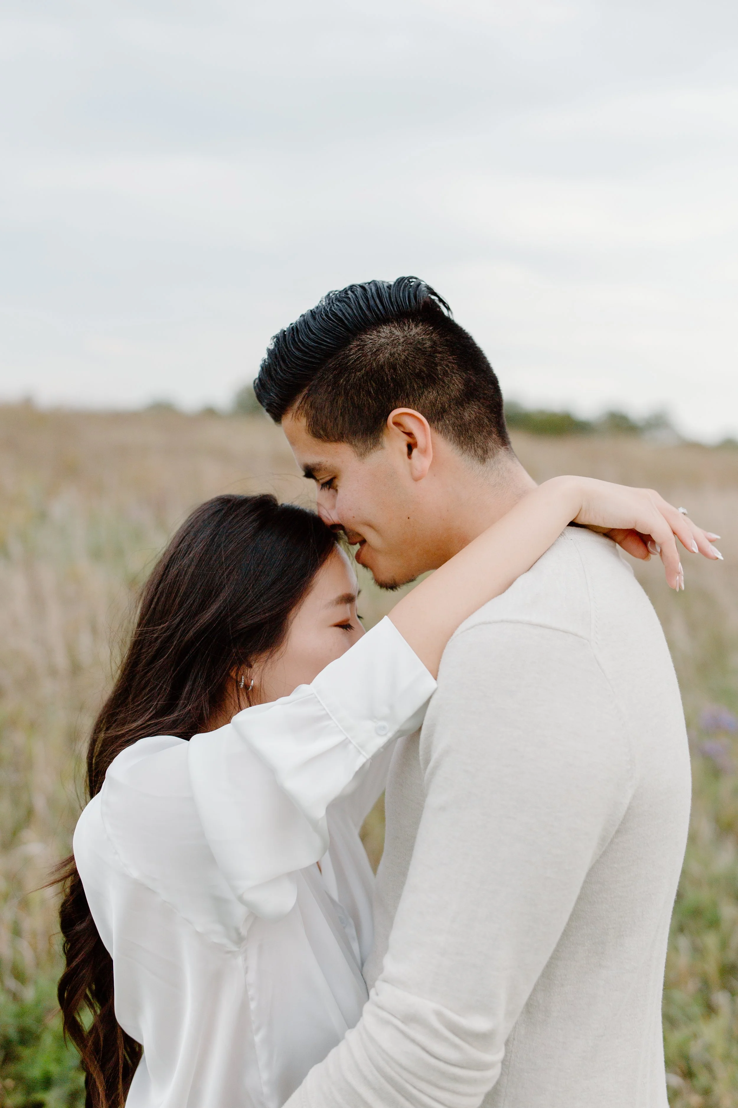 A close-up of a couple embracing outdoors, with their foreheads touching and eyes closed.