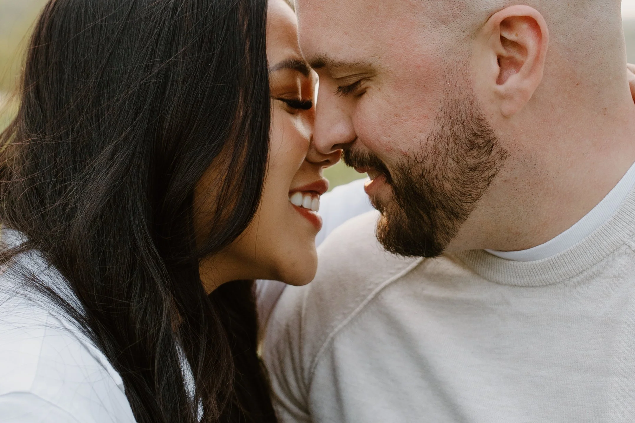 Close-up of a couple with foreheads touching, eyes closed, smiling, outdoors.