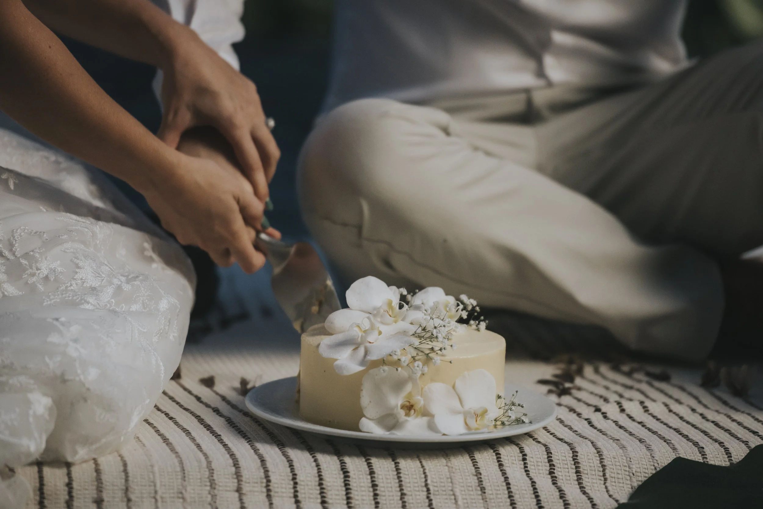Newlywed couple cutting a small, elegant wedding cake during their intimate rainforest elopement, surrounded by nature