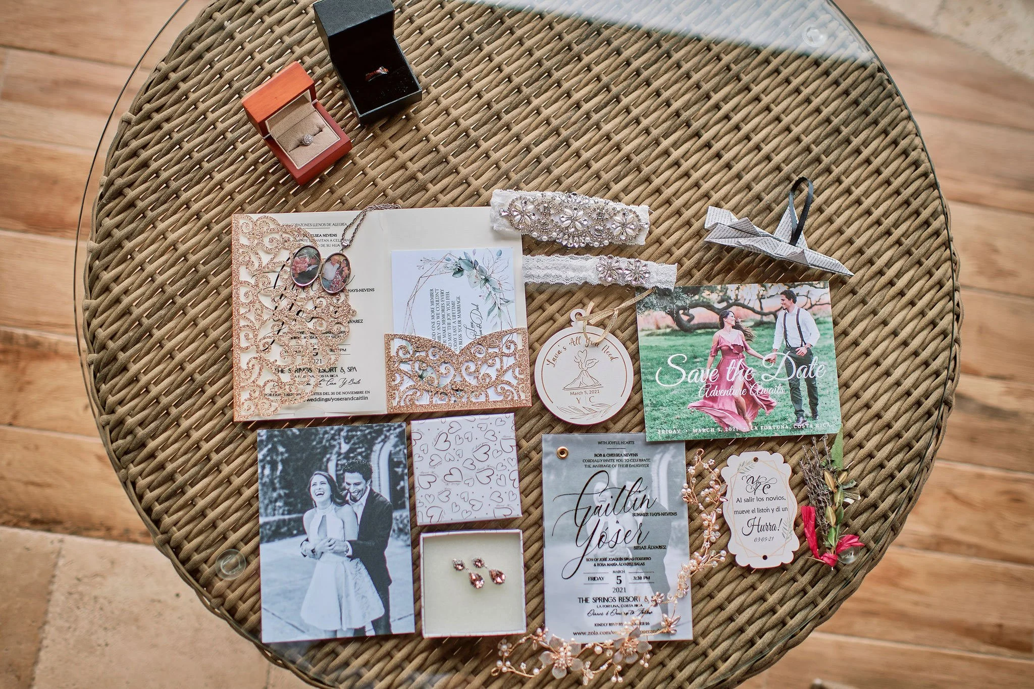 Close-up of wedding stationery surrounded by tropical leaves, rings and wedding favors