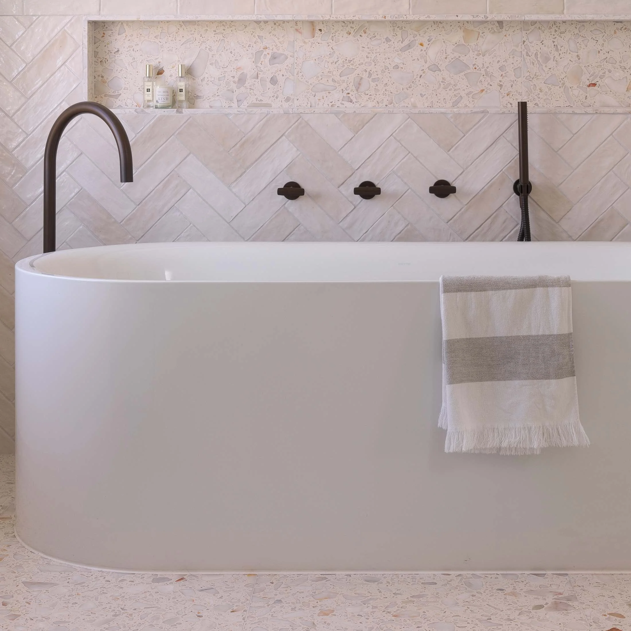 Dark bronze freestanding bath spout over freestanding white bath with towel hanging over bath.