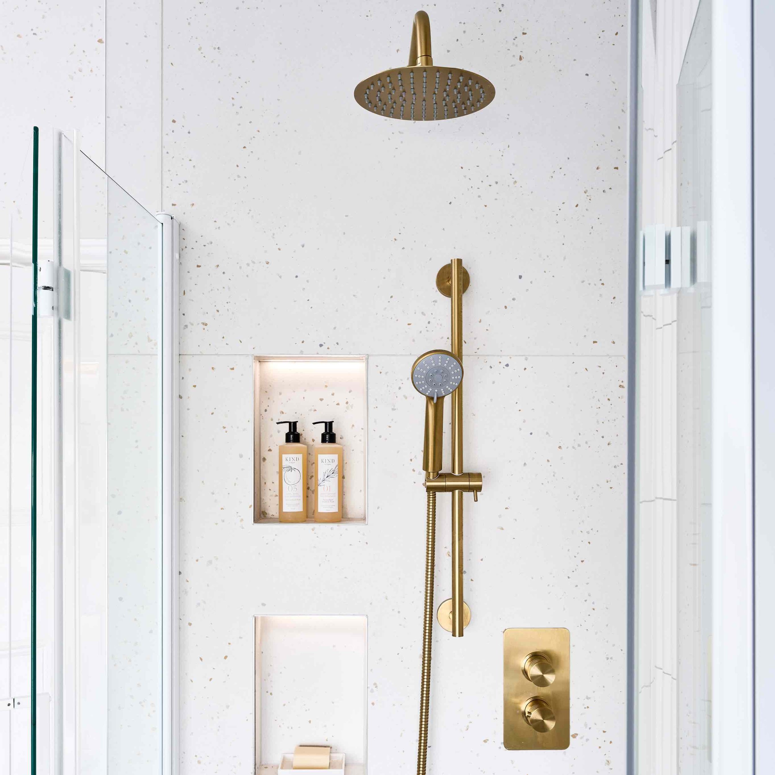 brushed brass bathroom shower in white tiled shower