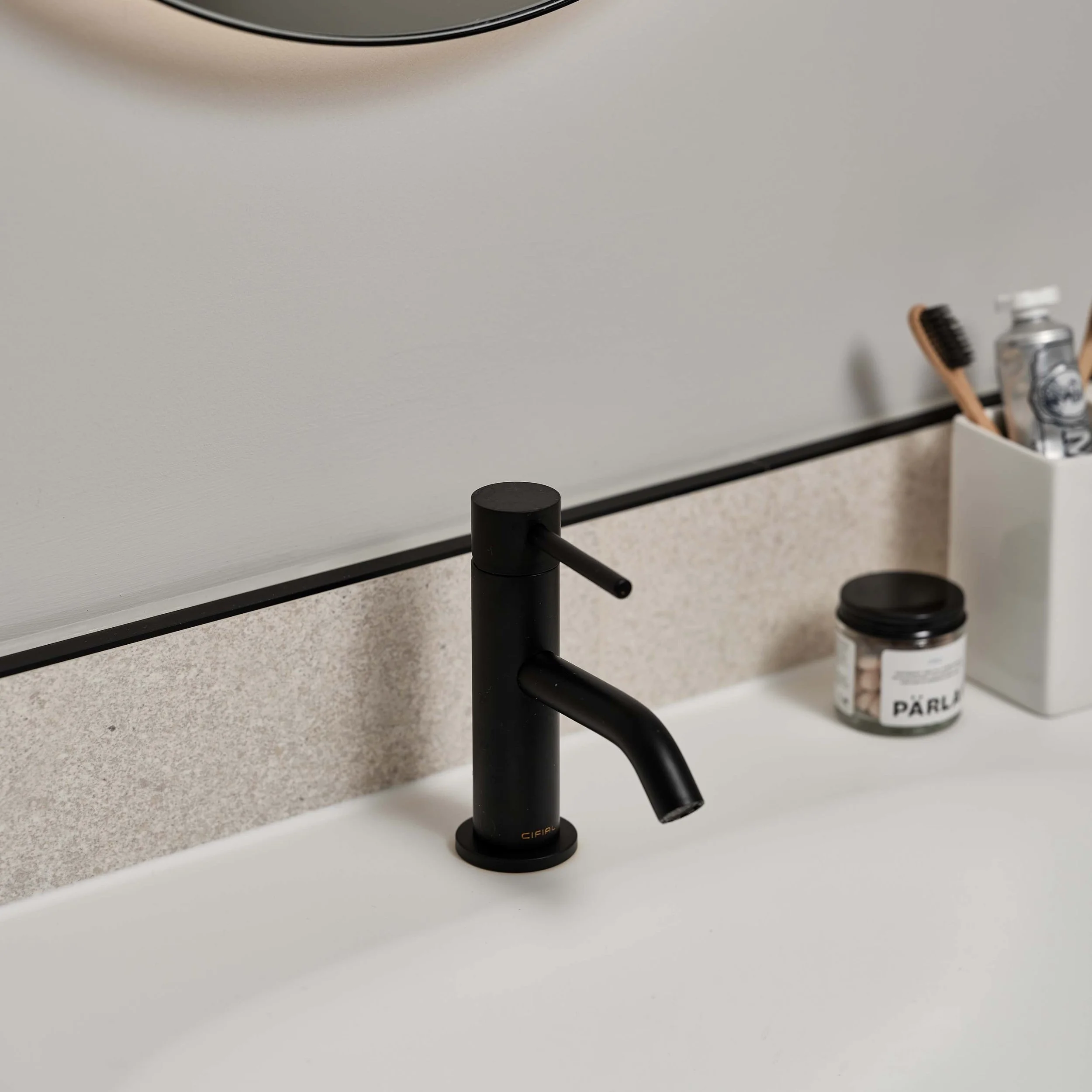 Black basin tap on a white basin with toothbrushes next to it on the right.