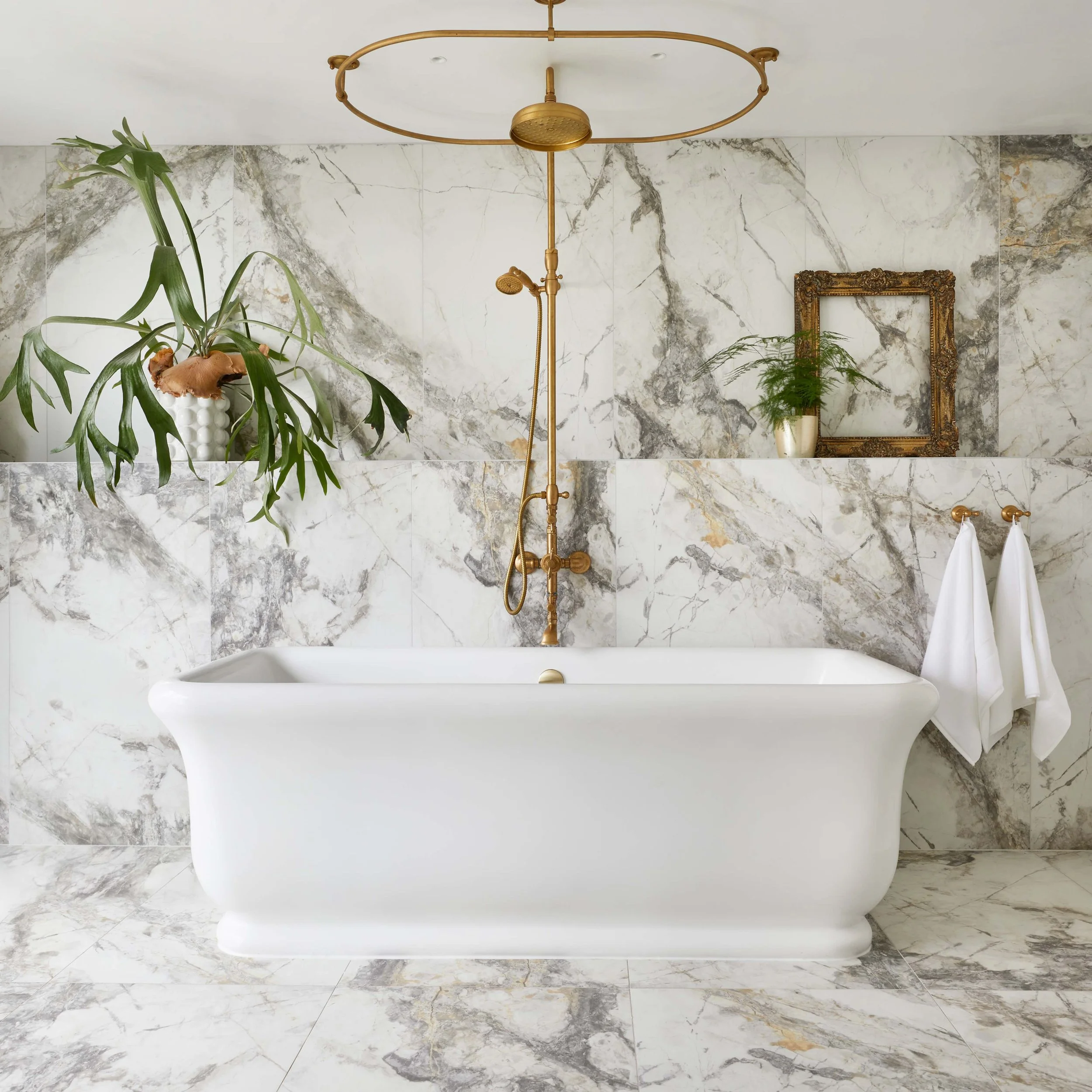 white marble bathroom with white bath and gold overhead shower